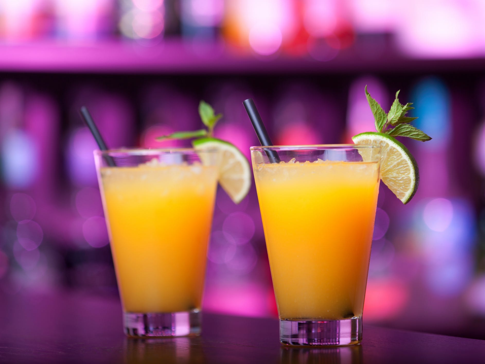 Two Harvey Wallbanger cocktails on a bar with a purple-lit background