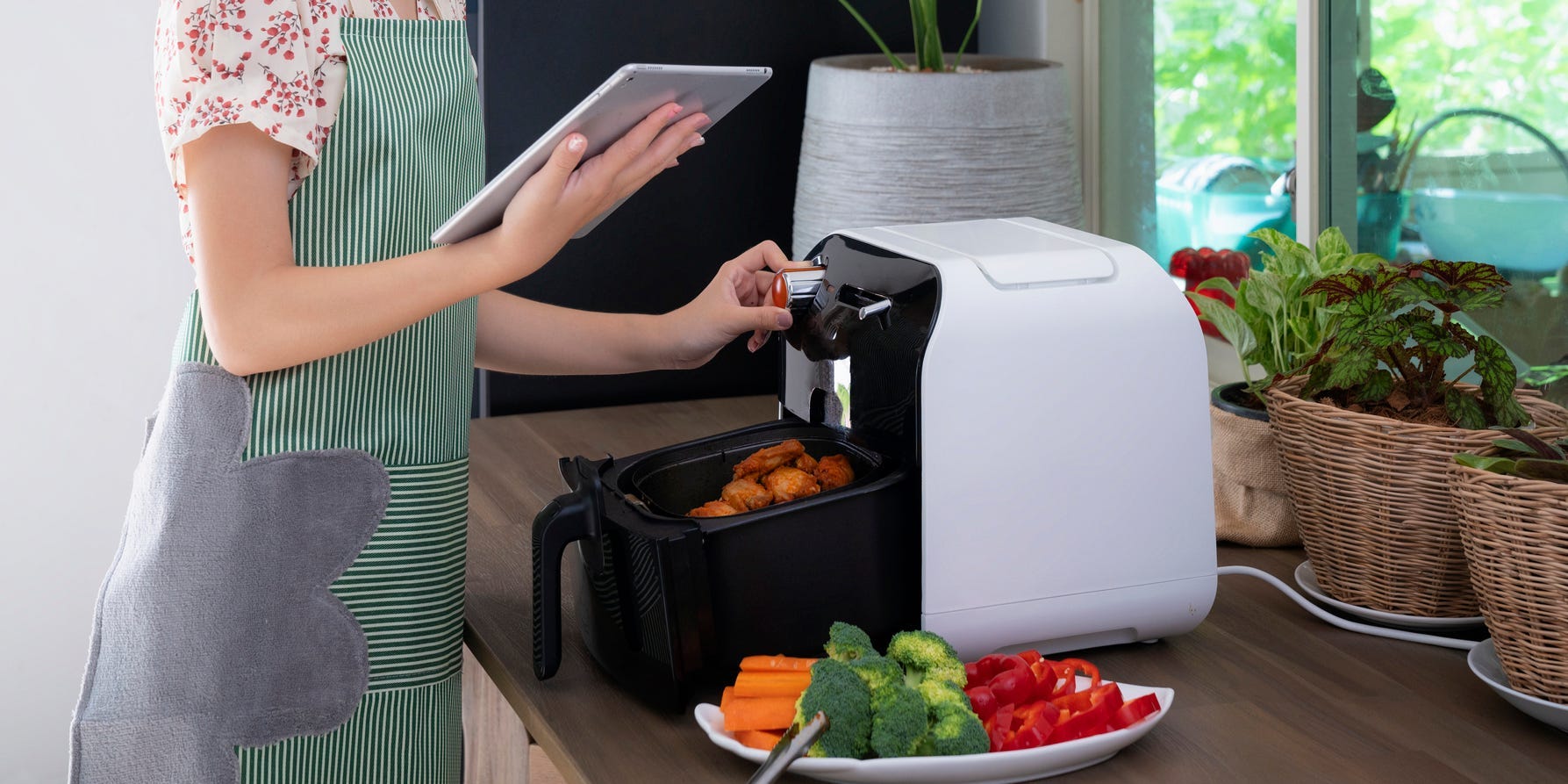 A woman checking a recipe on a tablet as she programs an air fryer