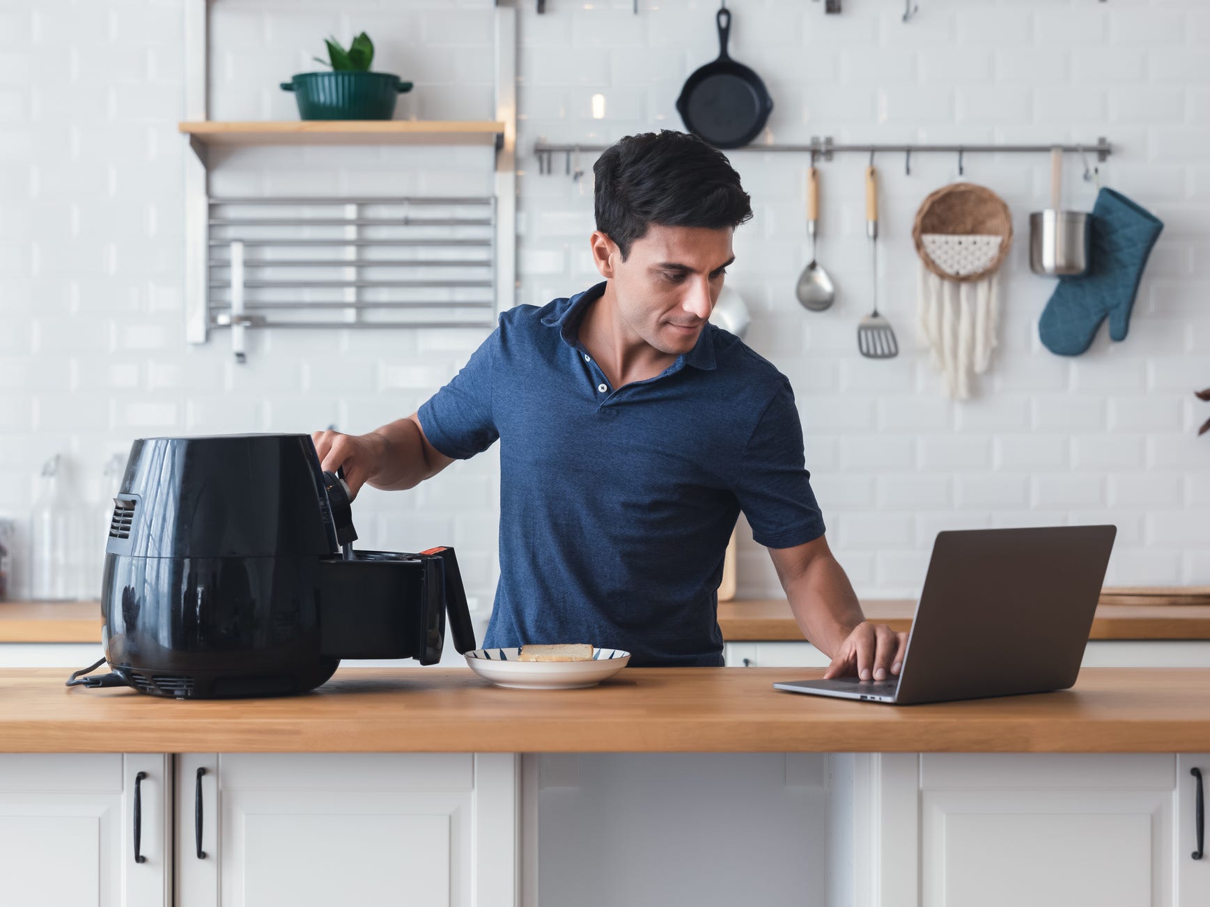 A man checking his laptop while he programs his air fryer