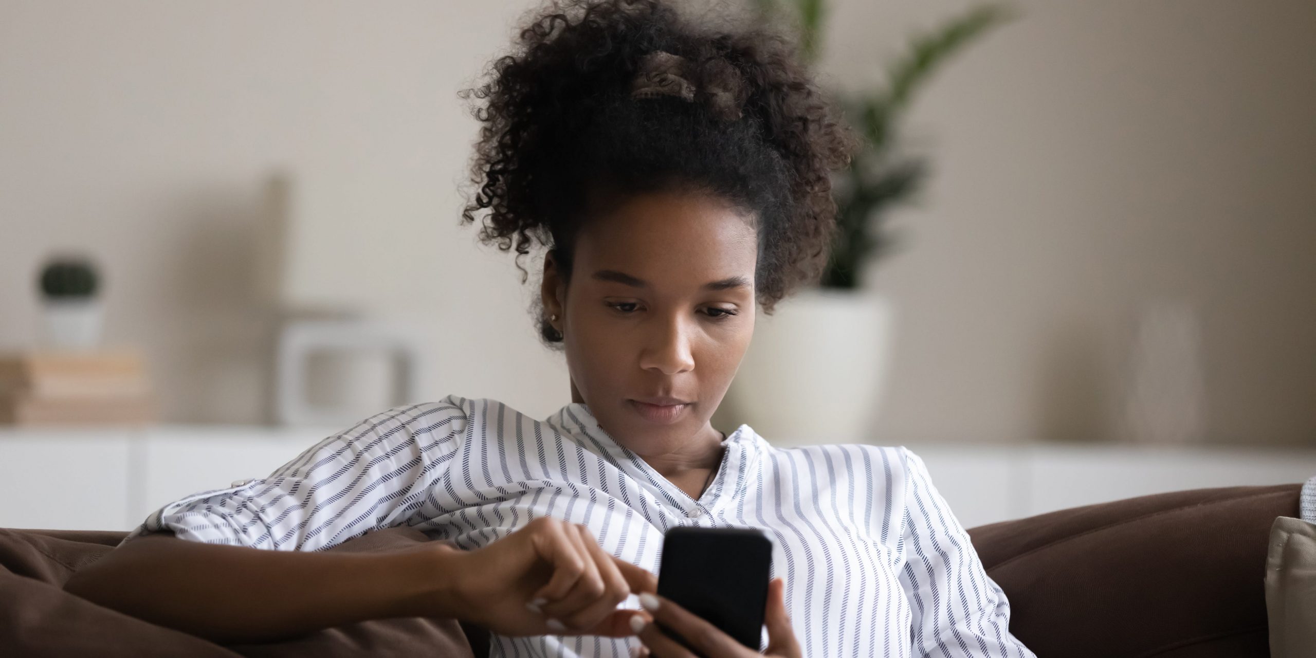 A young woman sits on a couch and looks at her phone.