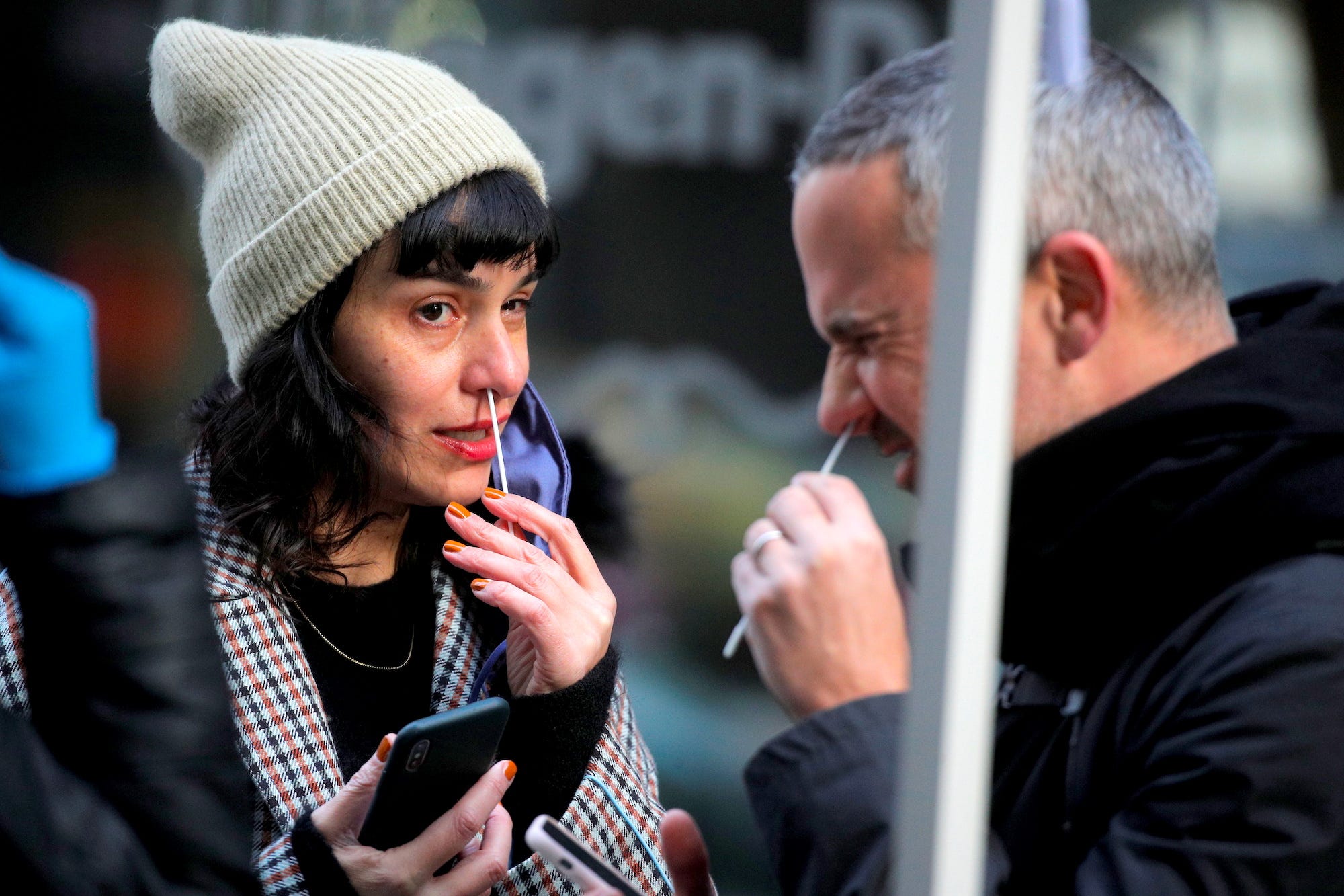 A man whinges while swabbing his nose for a covid test in New York City, USA on December 7, 2021, while a woman also swabbing her nose looks at him,