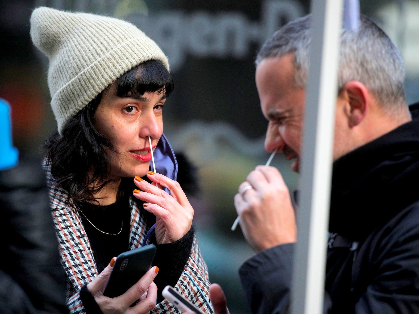 A man whinges while swabbing his nose for a covid test in New York City, USA on December 7, 2021, while a woman also swabbing her nose looks at him,