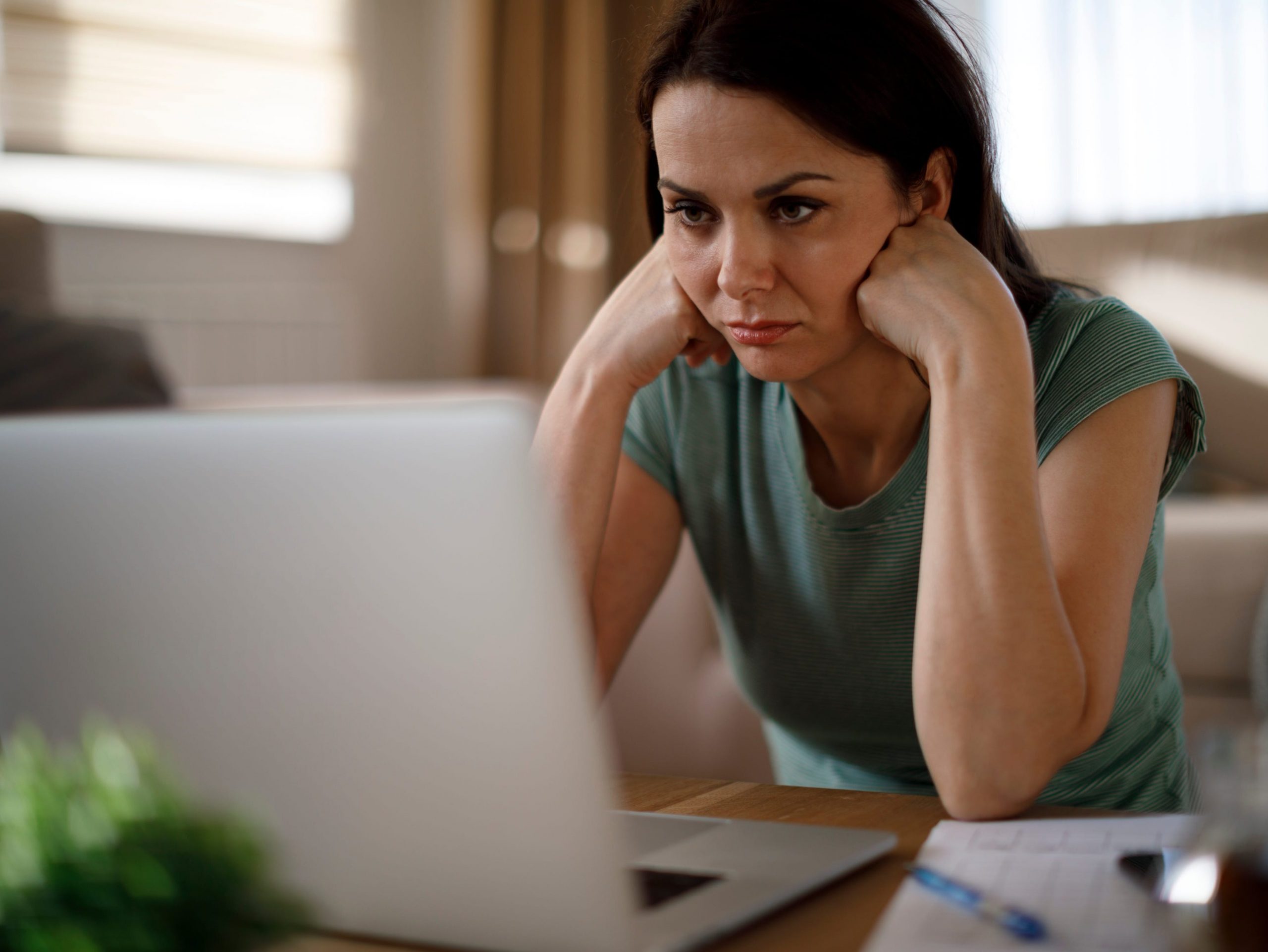 A woman looks sad as she stares at her laptop.