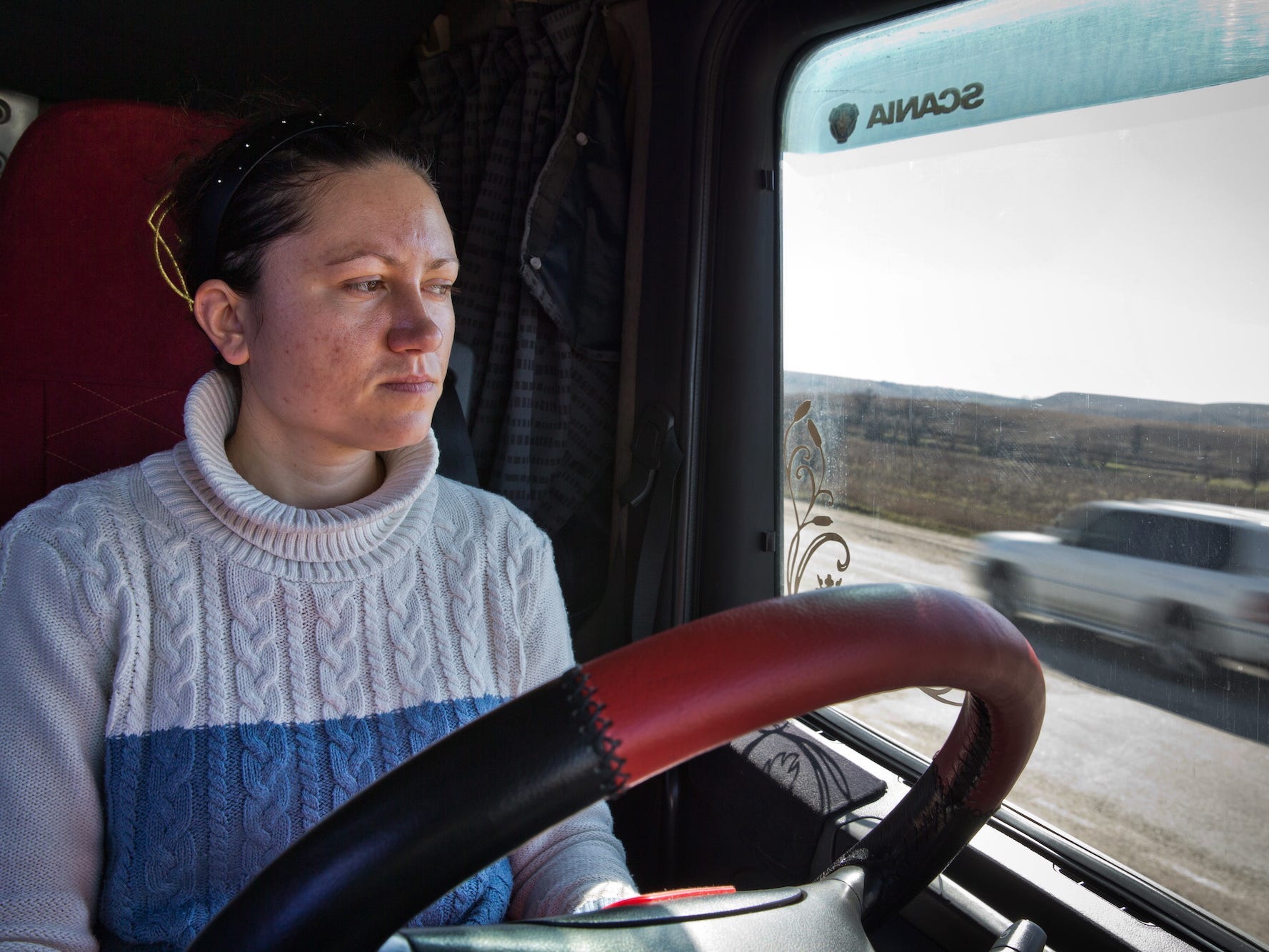 A female long-haul truck driver behind the wheel.