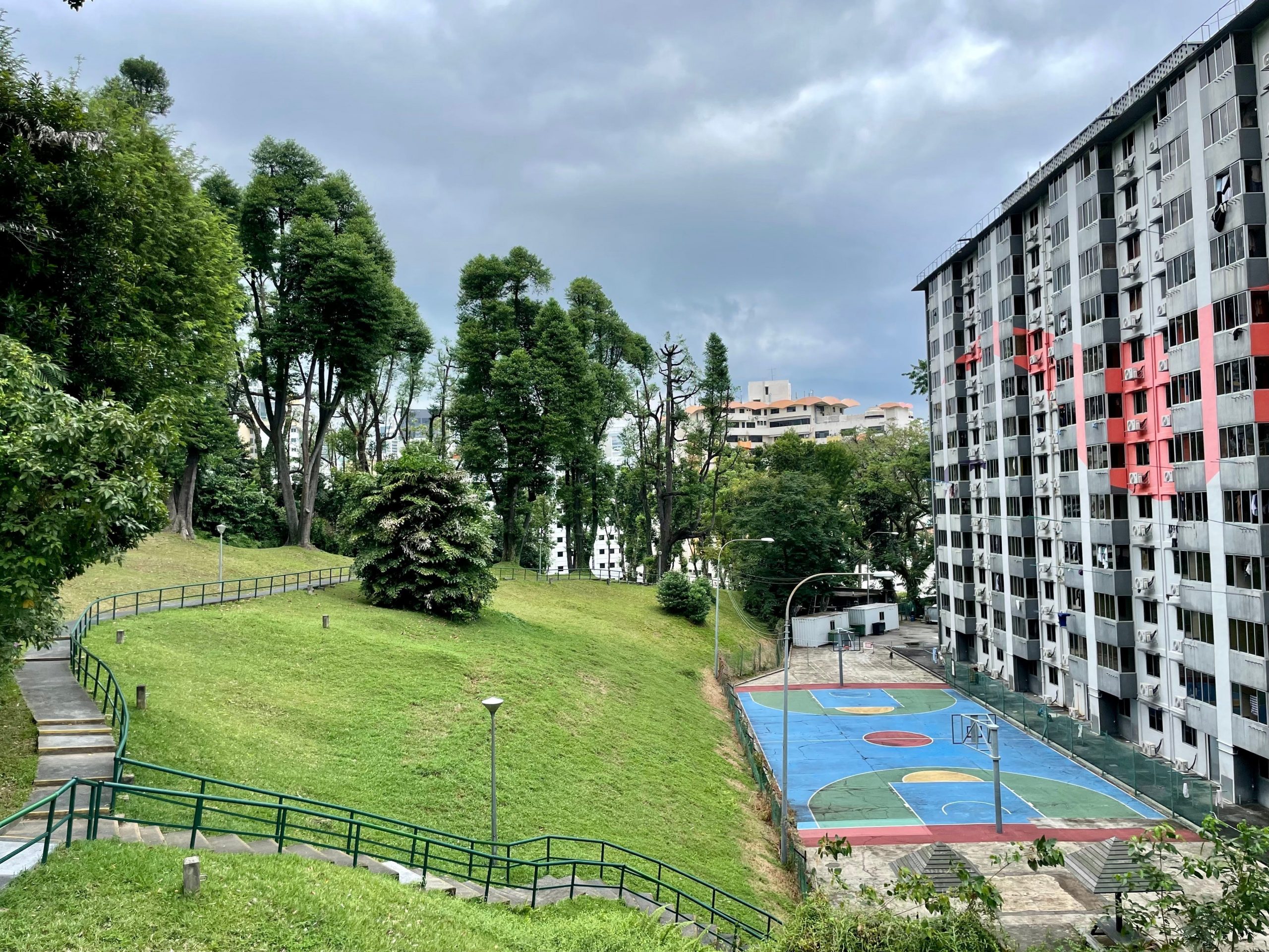 a large public housing unit in Singapore that's next to a hilly park and a basketball court