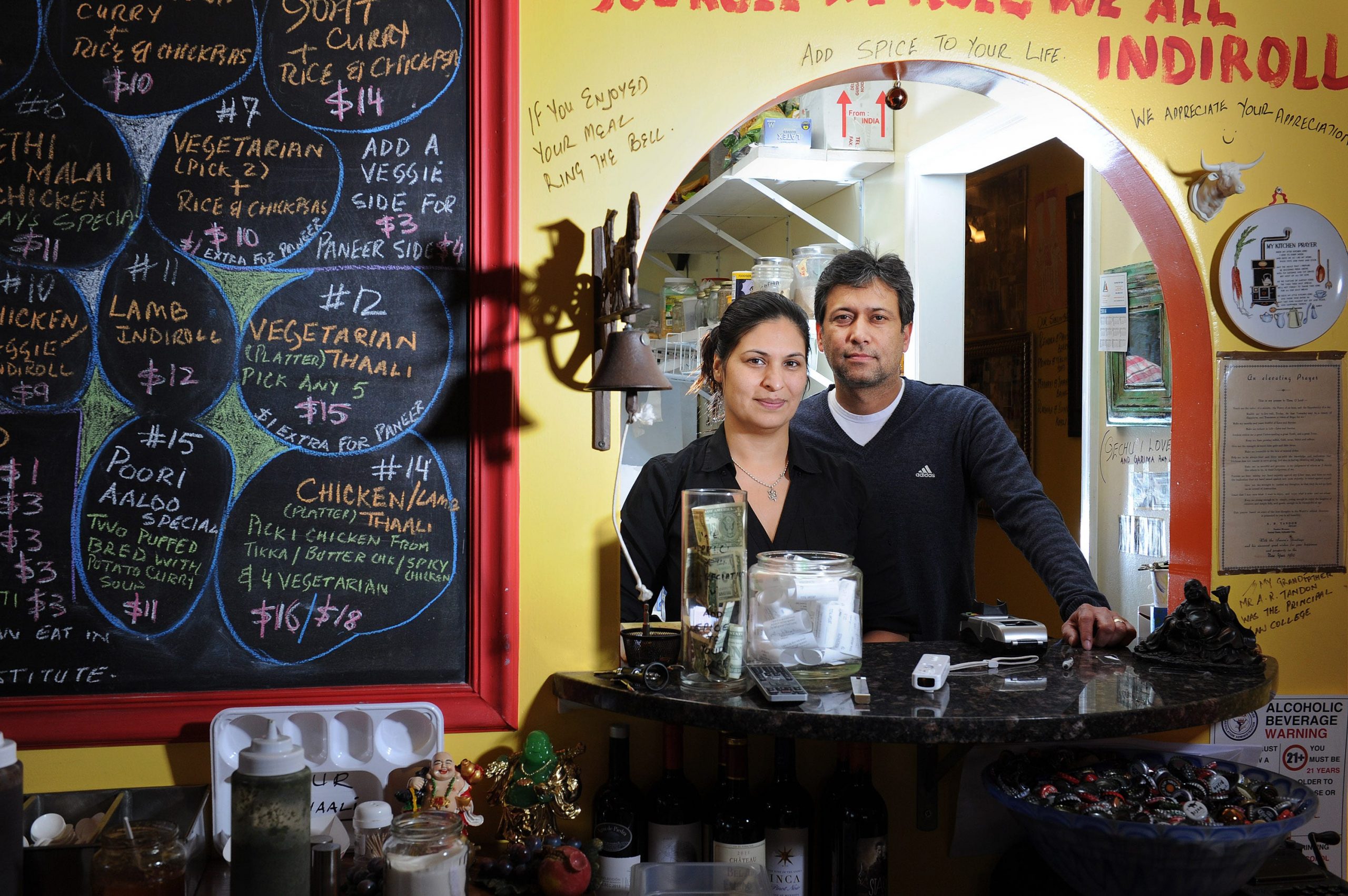 A man and a women stand together in a cramped brightly colored restaurant.