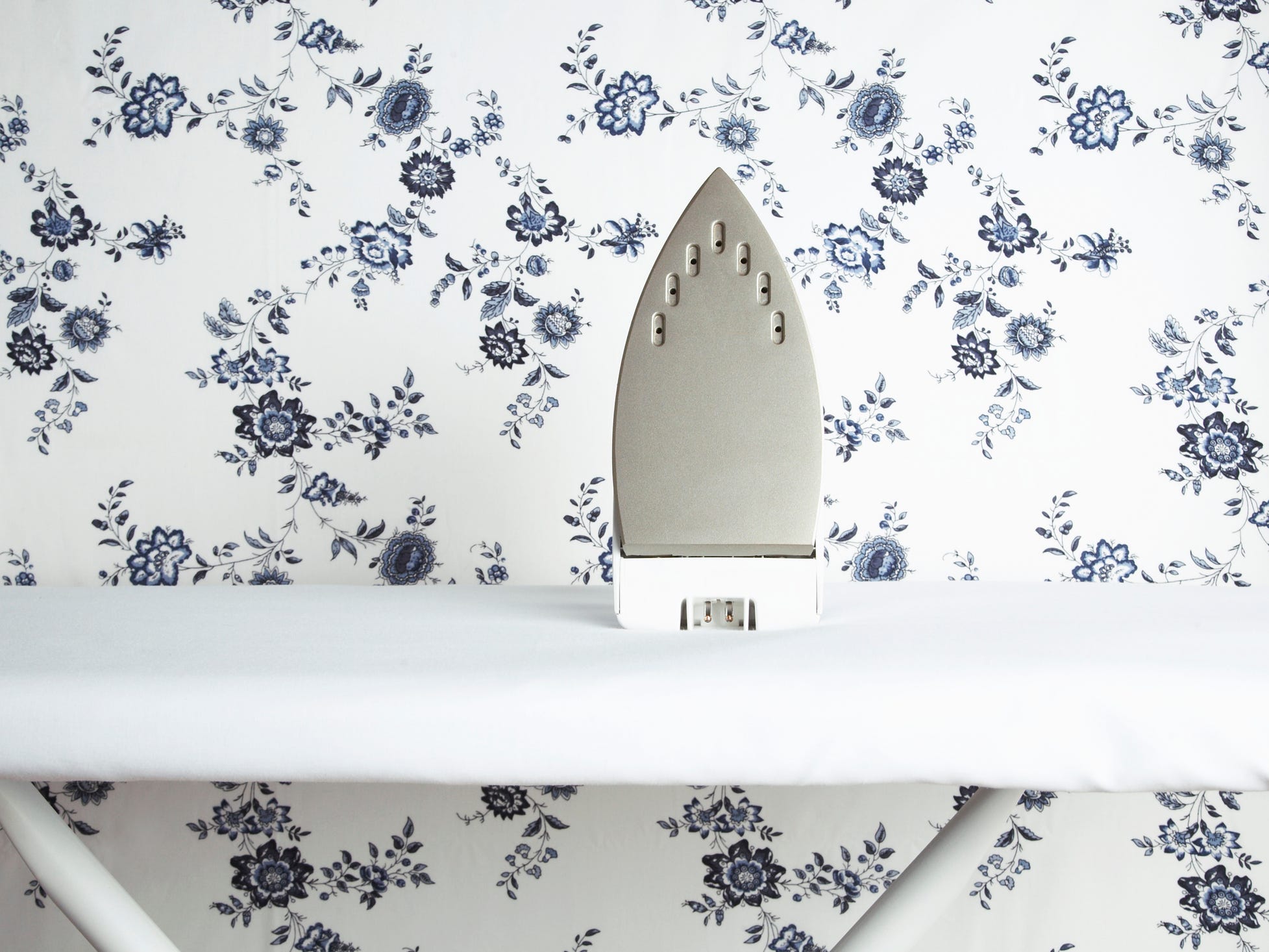 An iron sitting on an ironing board against a backdrop of floral wallpaper