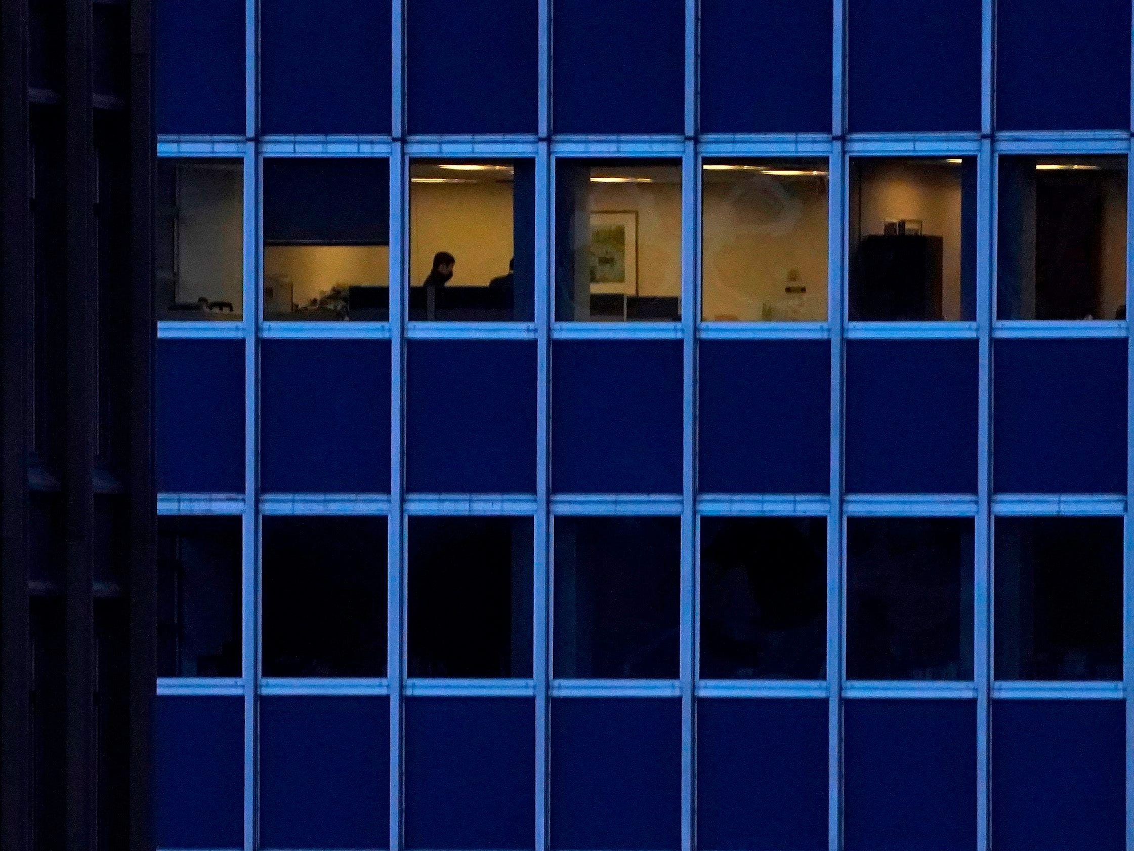 Person sits alone in lit-up office in mostly dark high-rise building in New York City