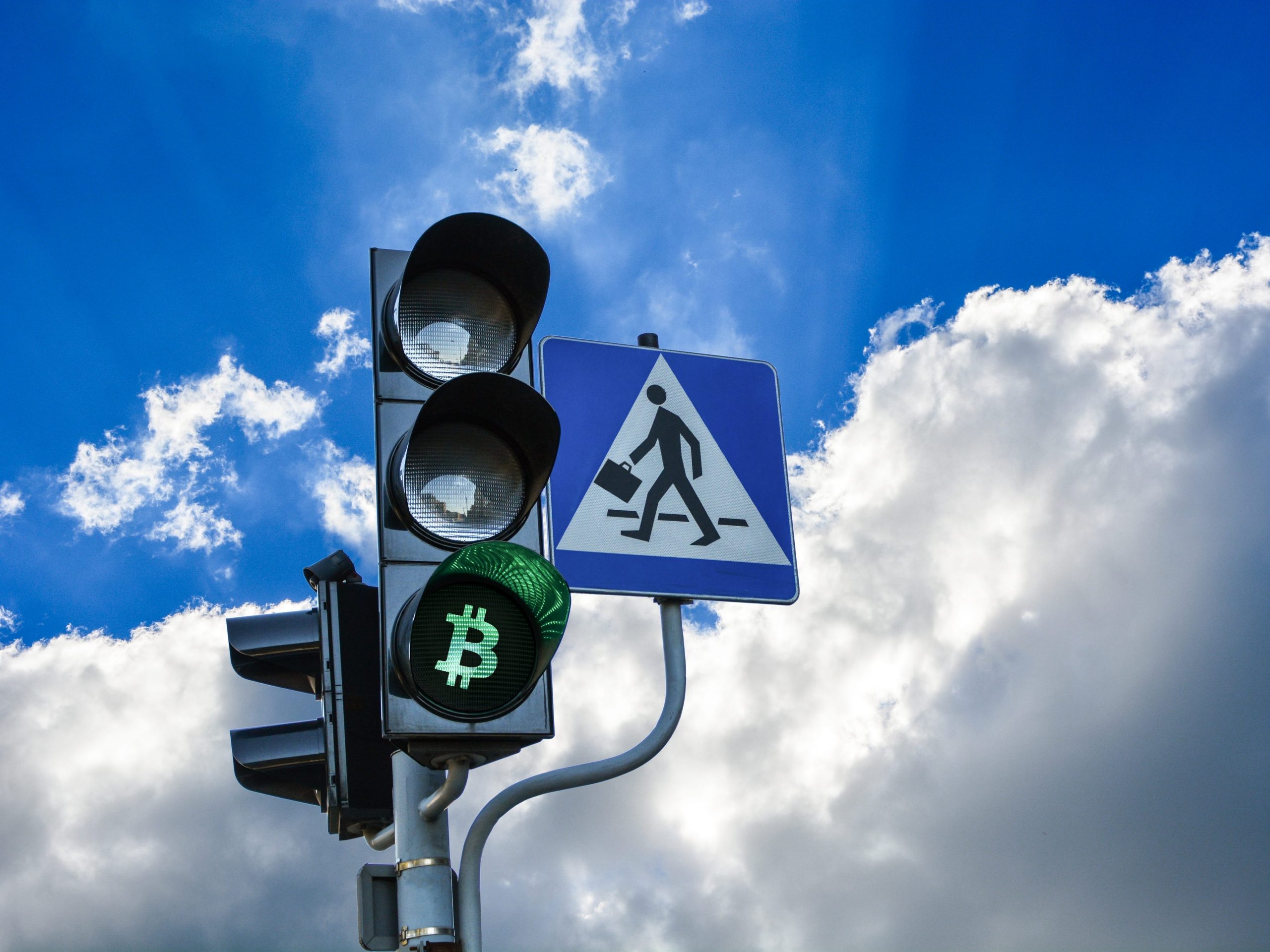 Traffic lights with green light replaced by bitcoin sign, clouds and light blue sky in the background