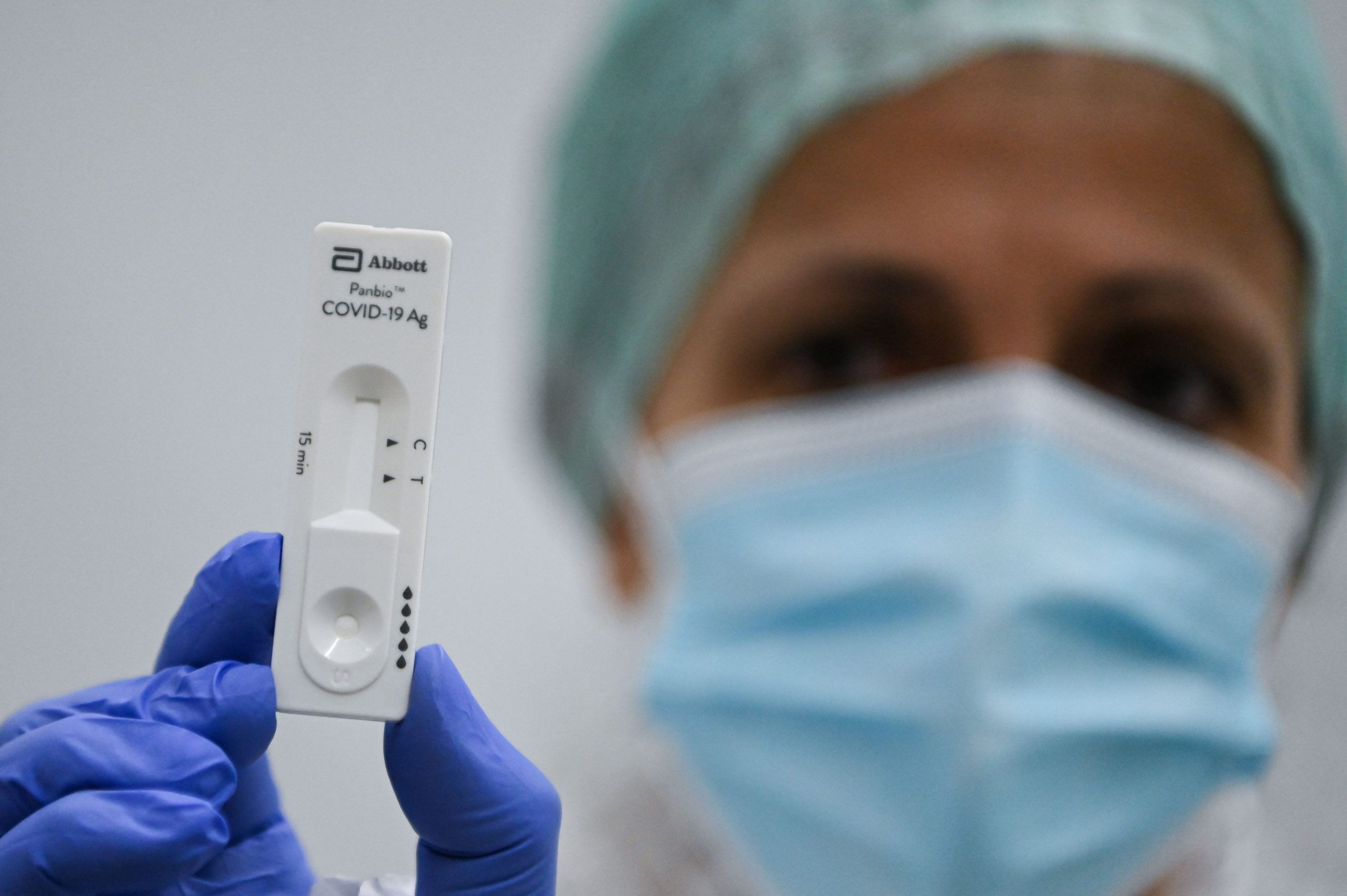 Women with mask, hat and gloves holds up rapid test.