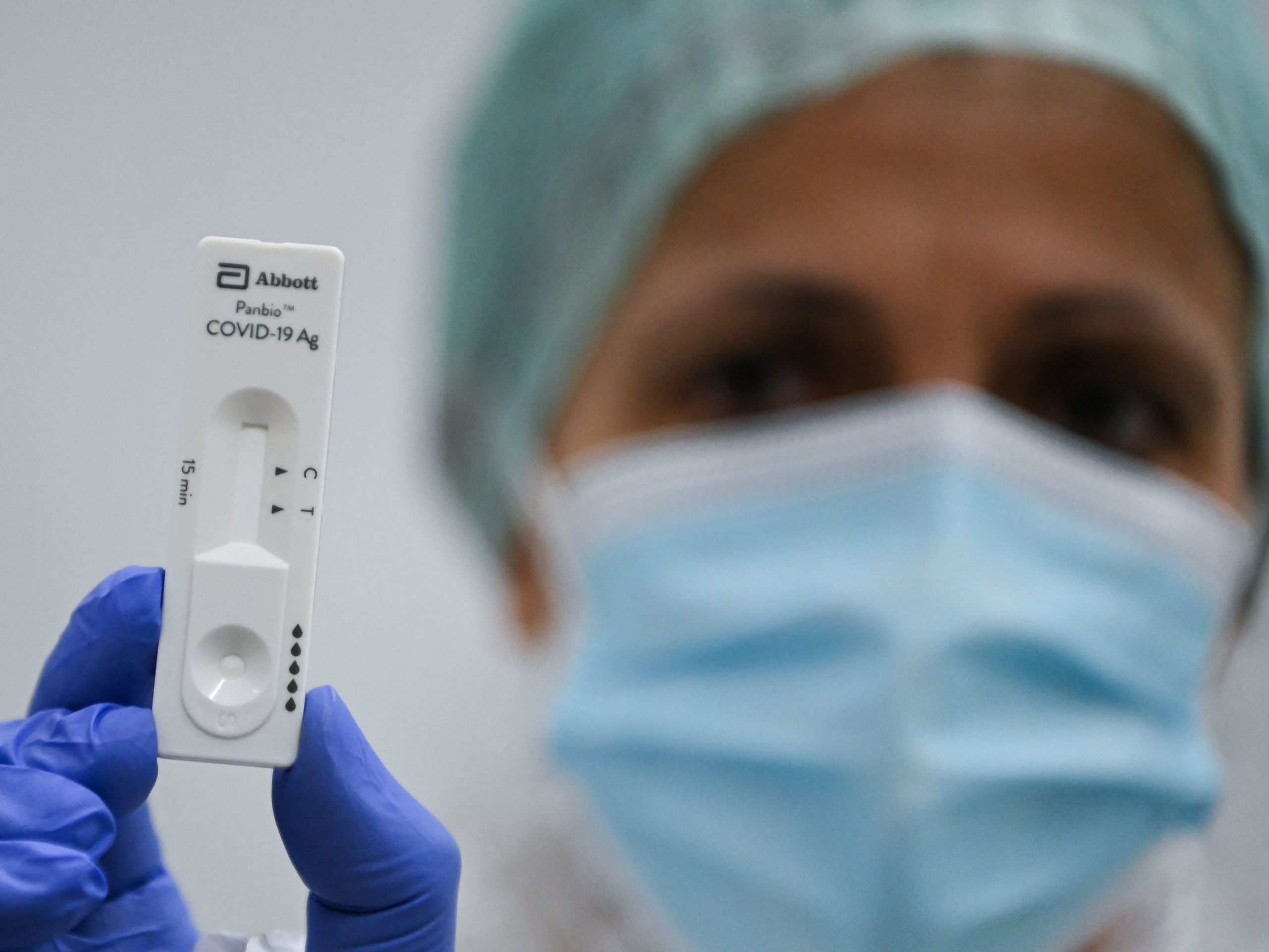 Women with mask, hat and gloves holds up rapid test.