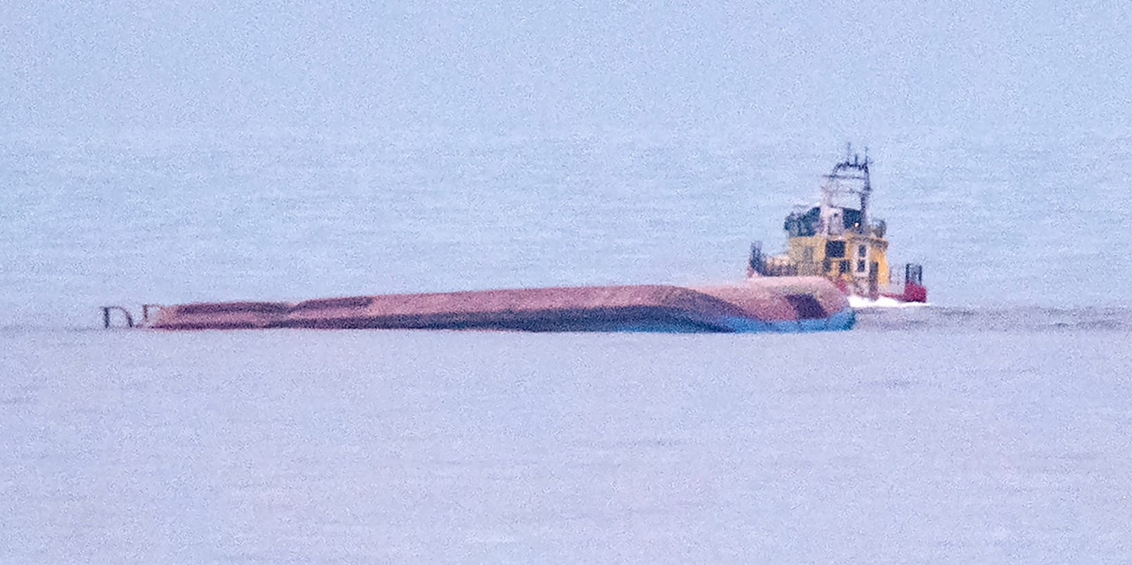 The hull of the overturned Karin Hoej in the Baltic Sea with e rescue vessel behind it, December 2021