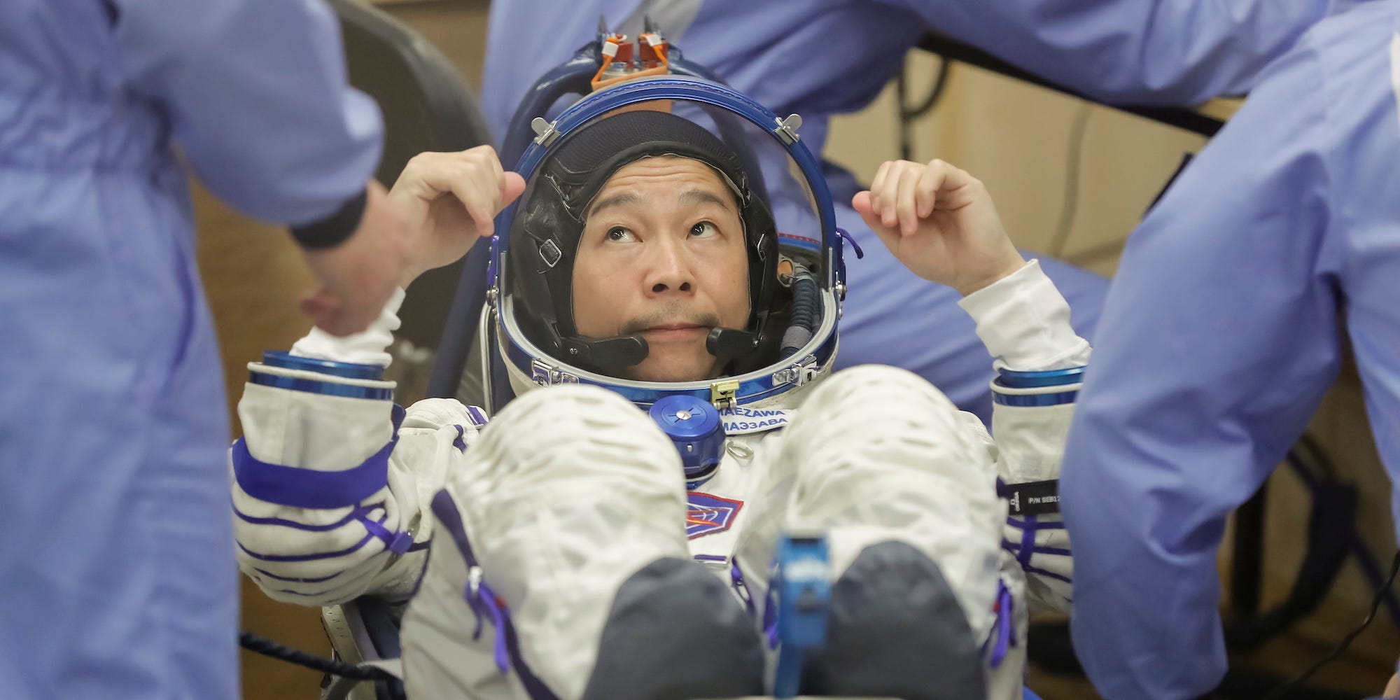 Yusaku Maezawa in a space suit, looking at people as they check its fit