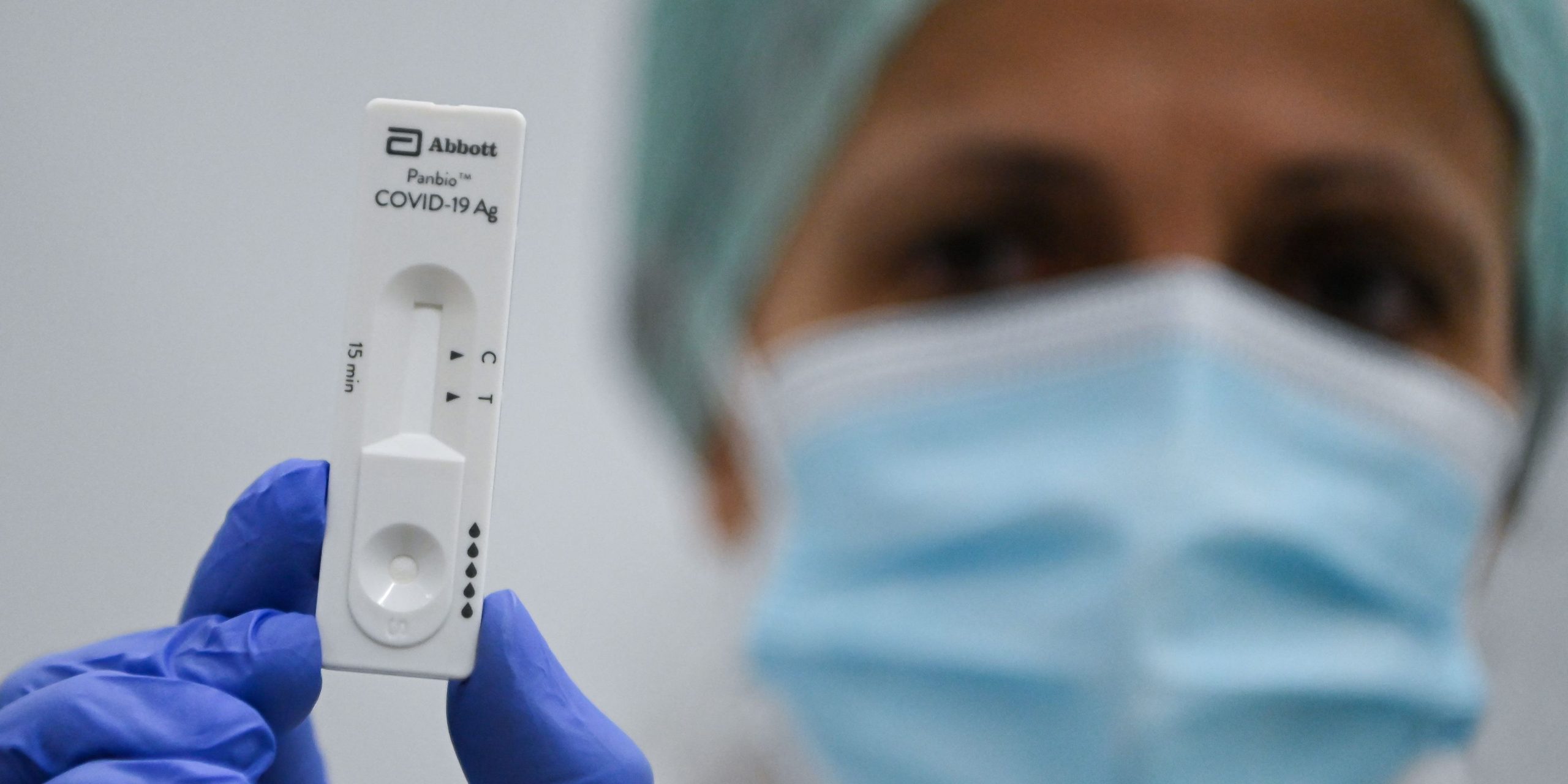 Women with mask, hat and gloves holds up rapid test.