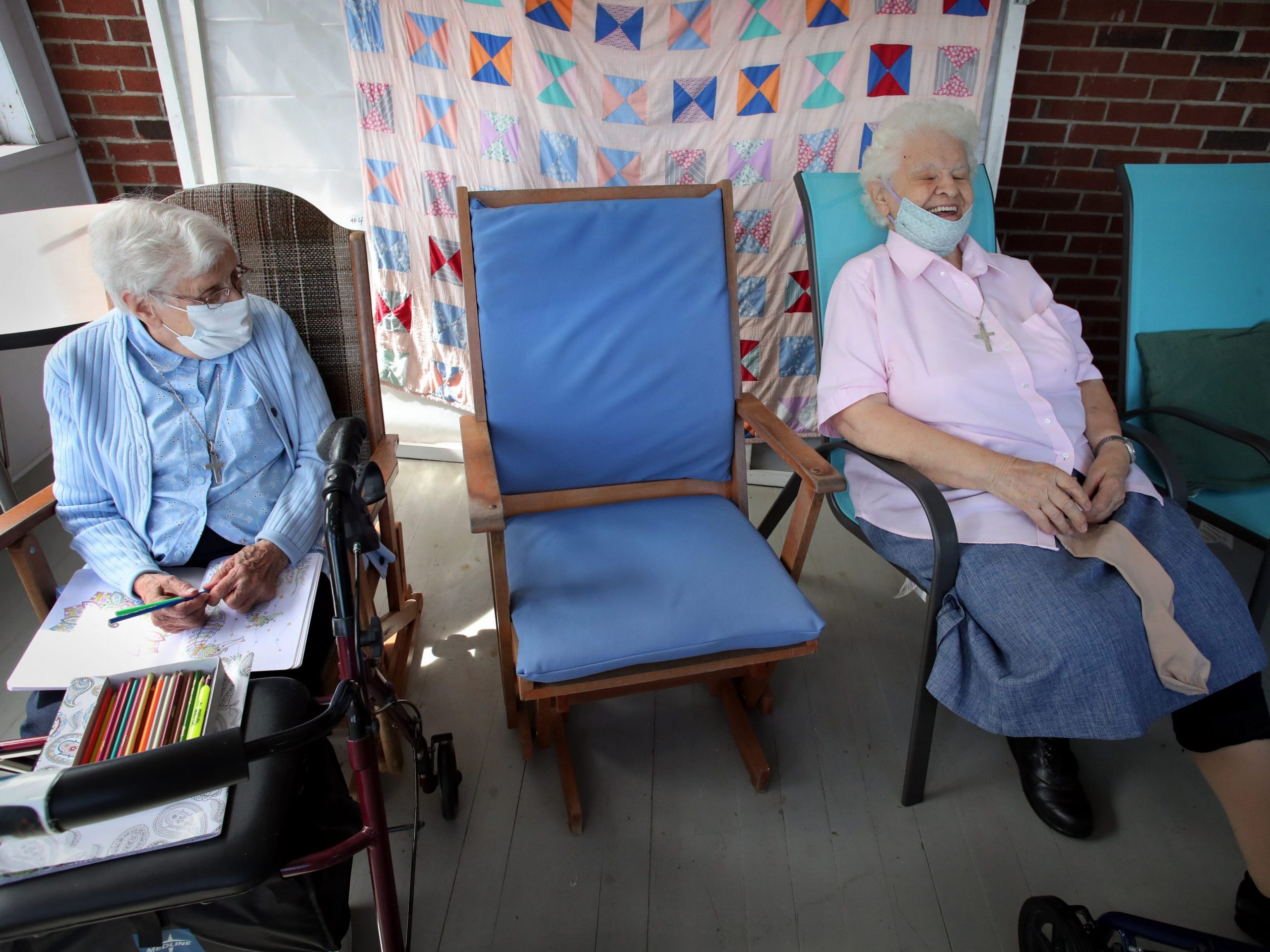 Two elderly women who have social distance between them laugh together.