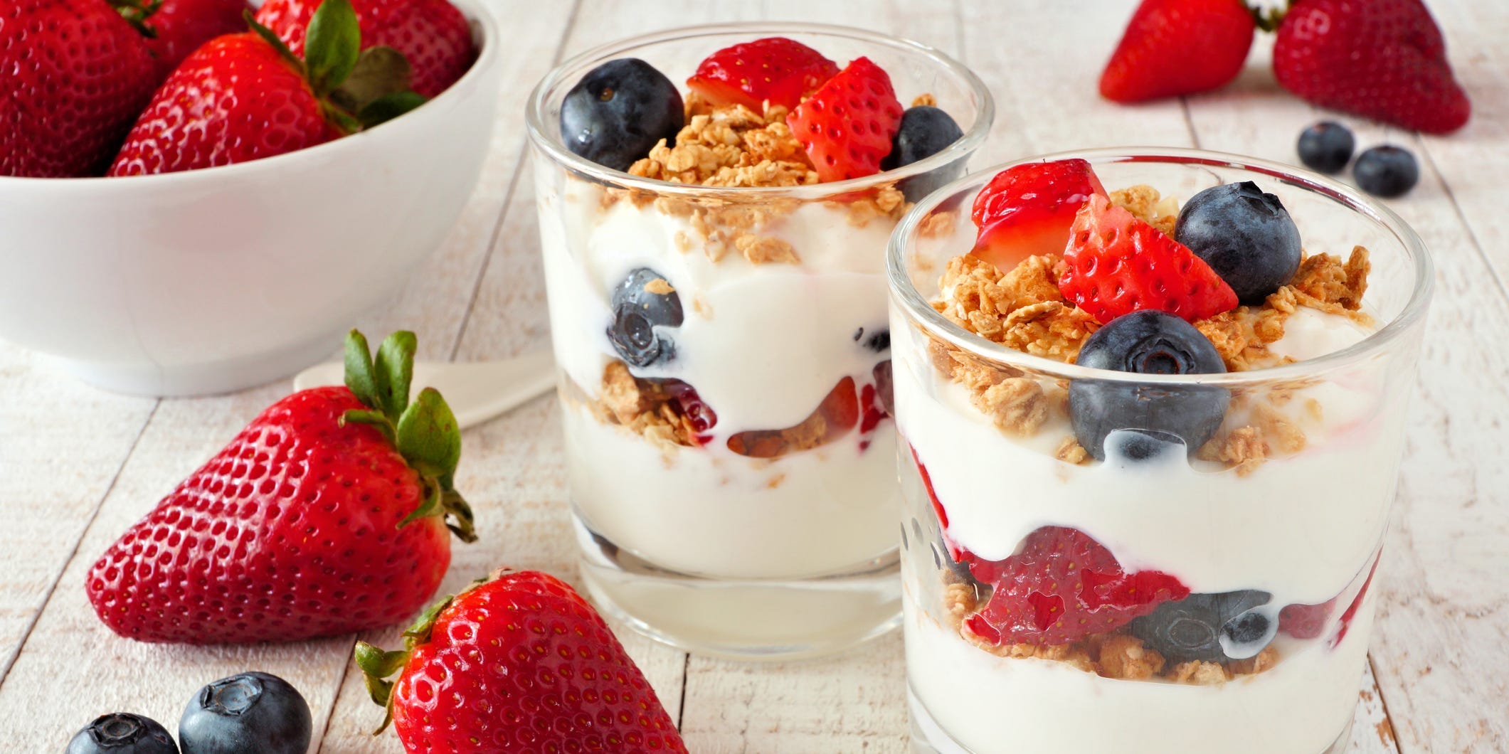 Two strawberry and blueberry yogurt parfaits in clear glasses surrounded by whole strawberries