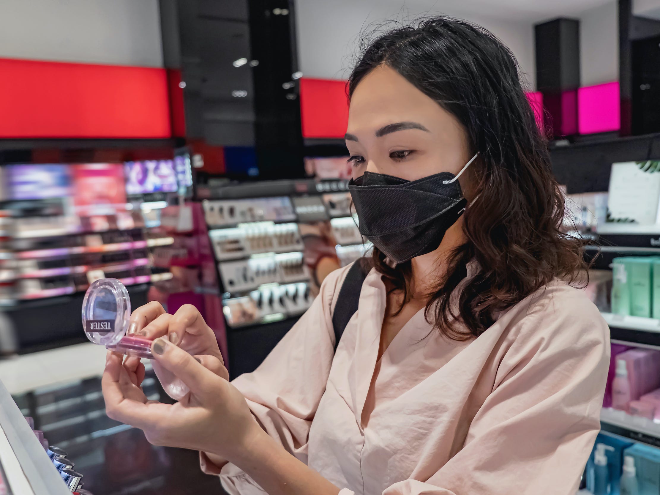 Woman wearing a mask tests cream blush at makeup store