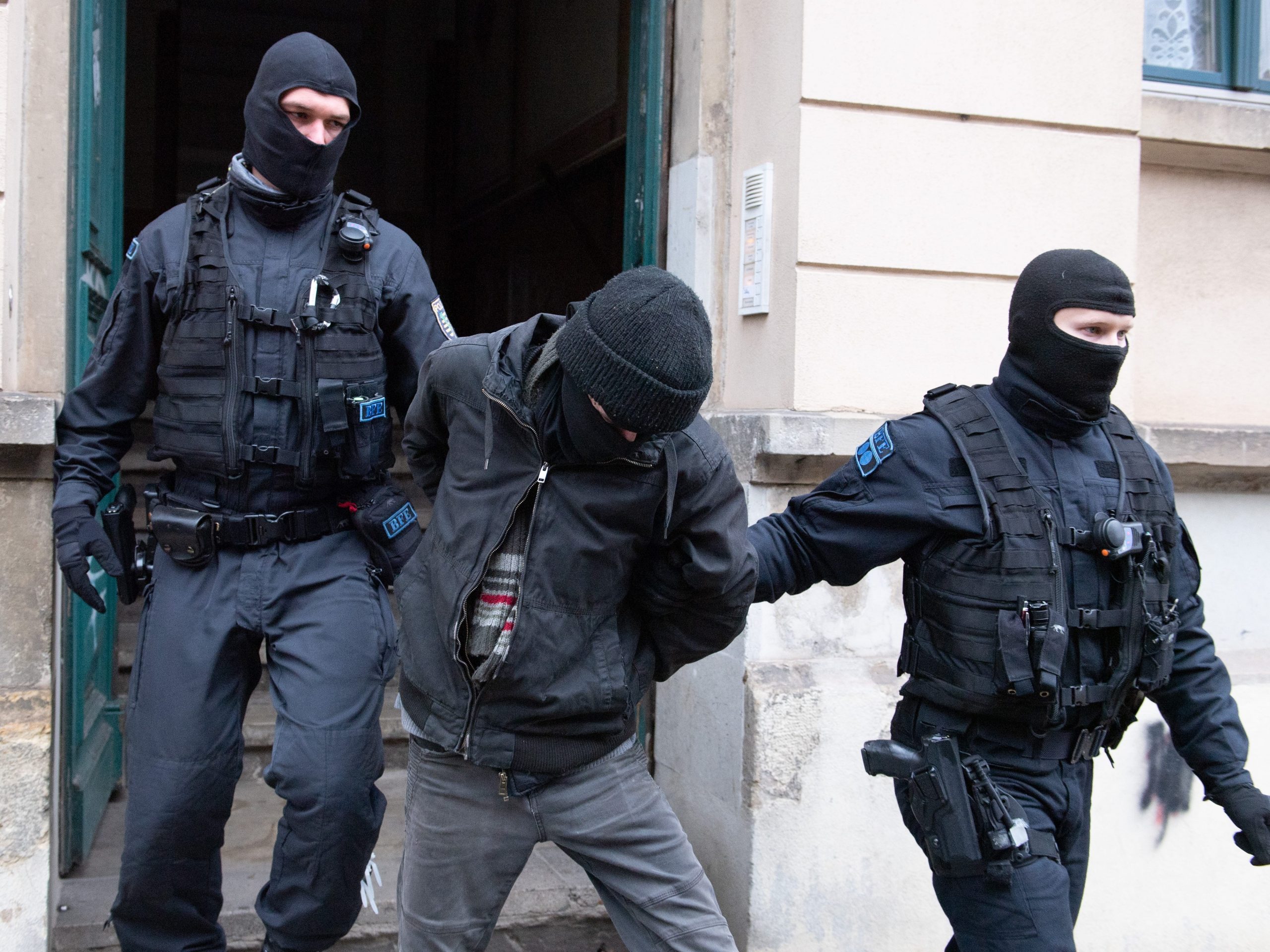 Police officers lead a suspect out of a building entrance during a raid in the Pieschen district on December 15, 2021, in Saxony, Dresden.