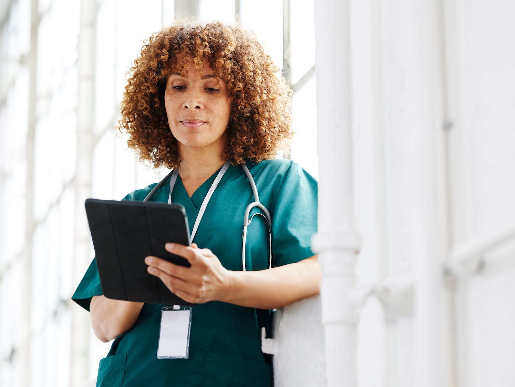 Female healthcare professional standing by windows and reading a digital tablet