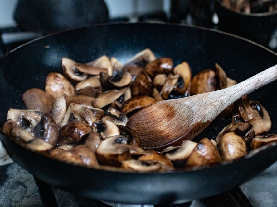 Sauteed mushrooms in a frying pan with a wooden spoon.