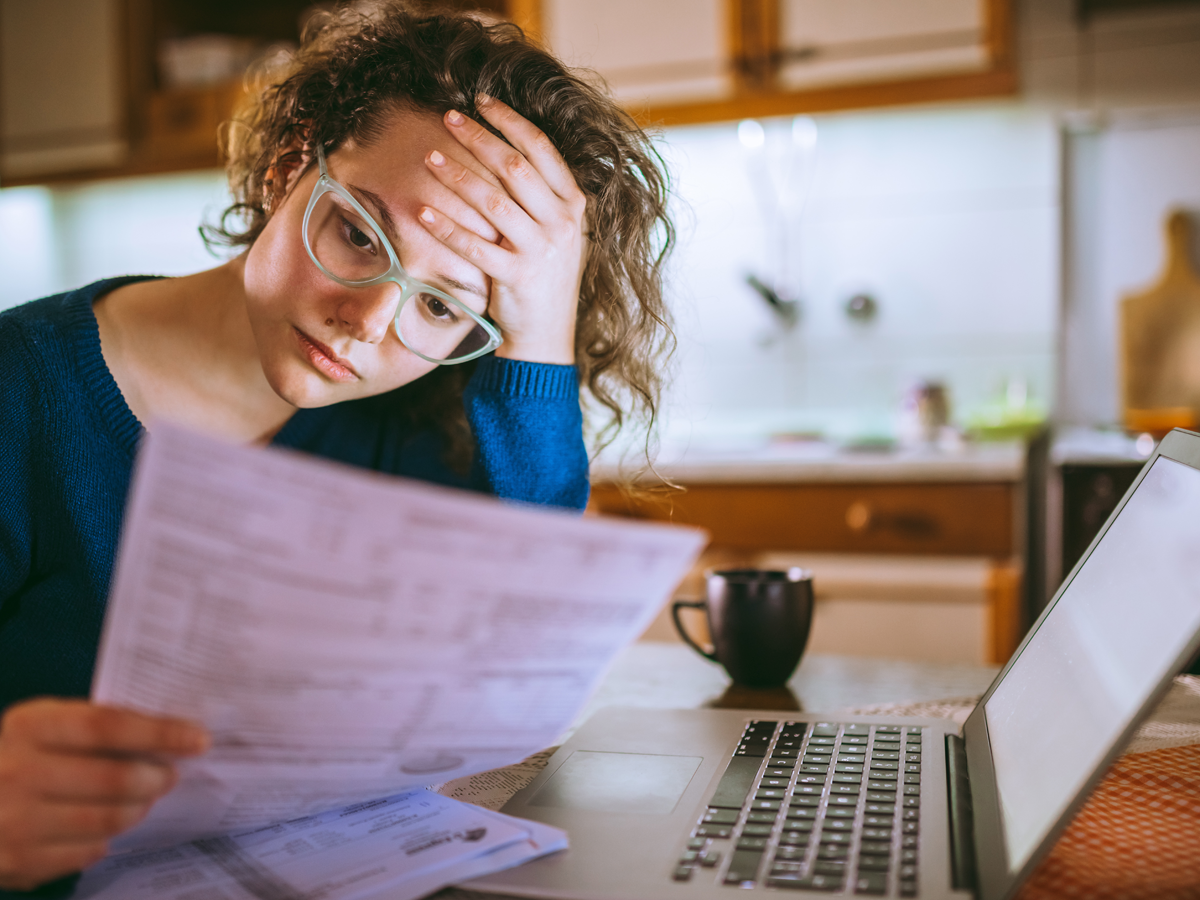 A photo of a young woman with a tax form in front of a laptop computer looking stressed.