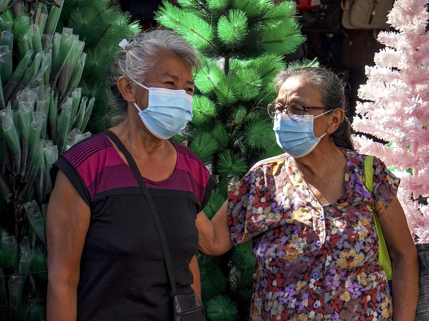 Two older women wearing masks are pictured in front of Christmas trees on December 14, 2021 in San Salvador, El Salvador.