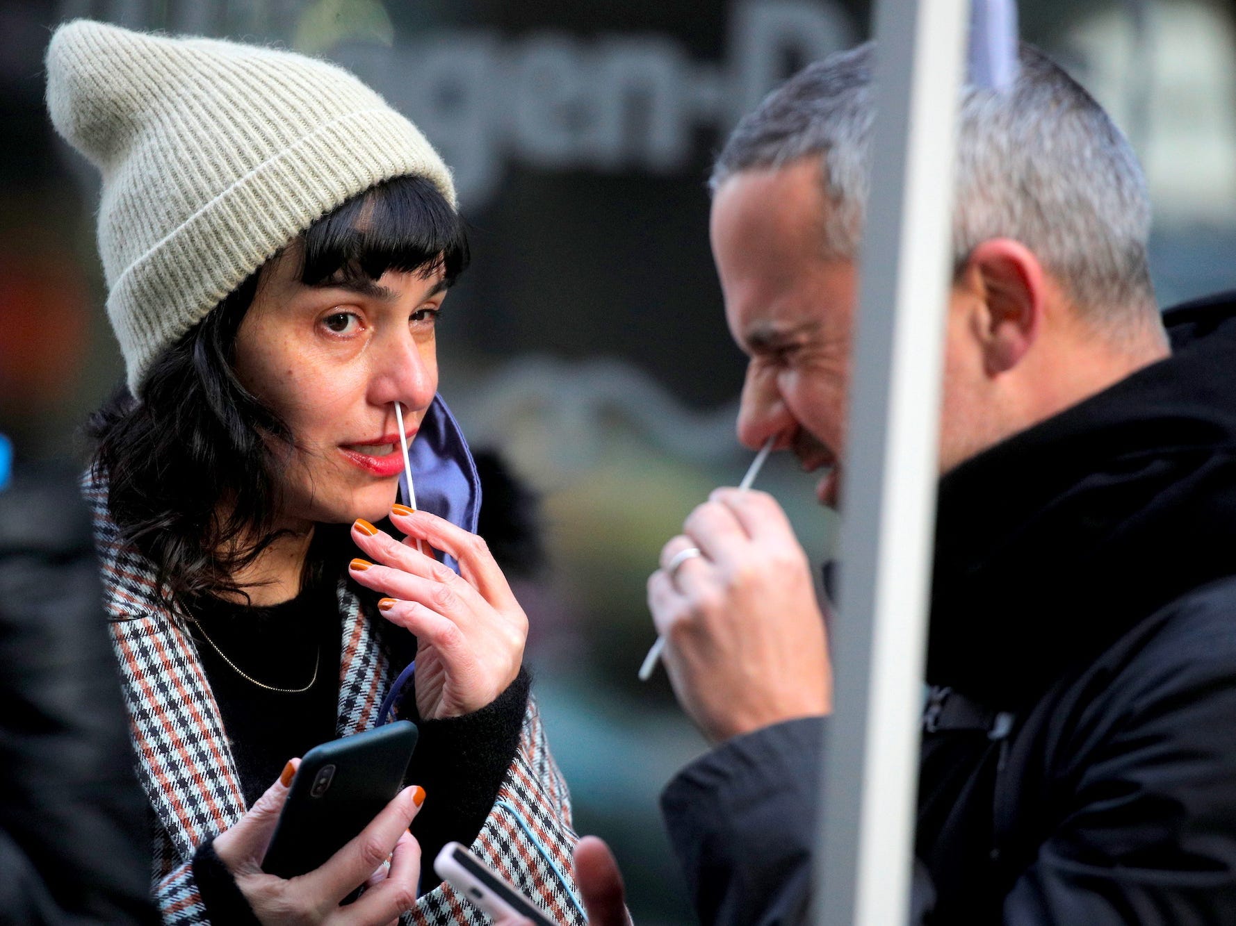 A man whinces while swabbing his nose for a covid test in New York City, USA on December 7, 2021, while a woman also swabbing her nose looks at him,