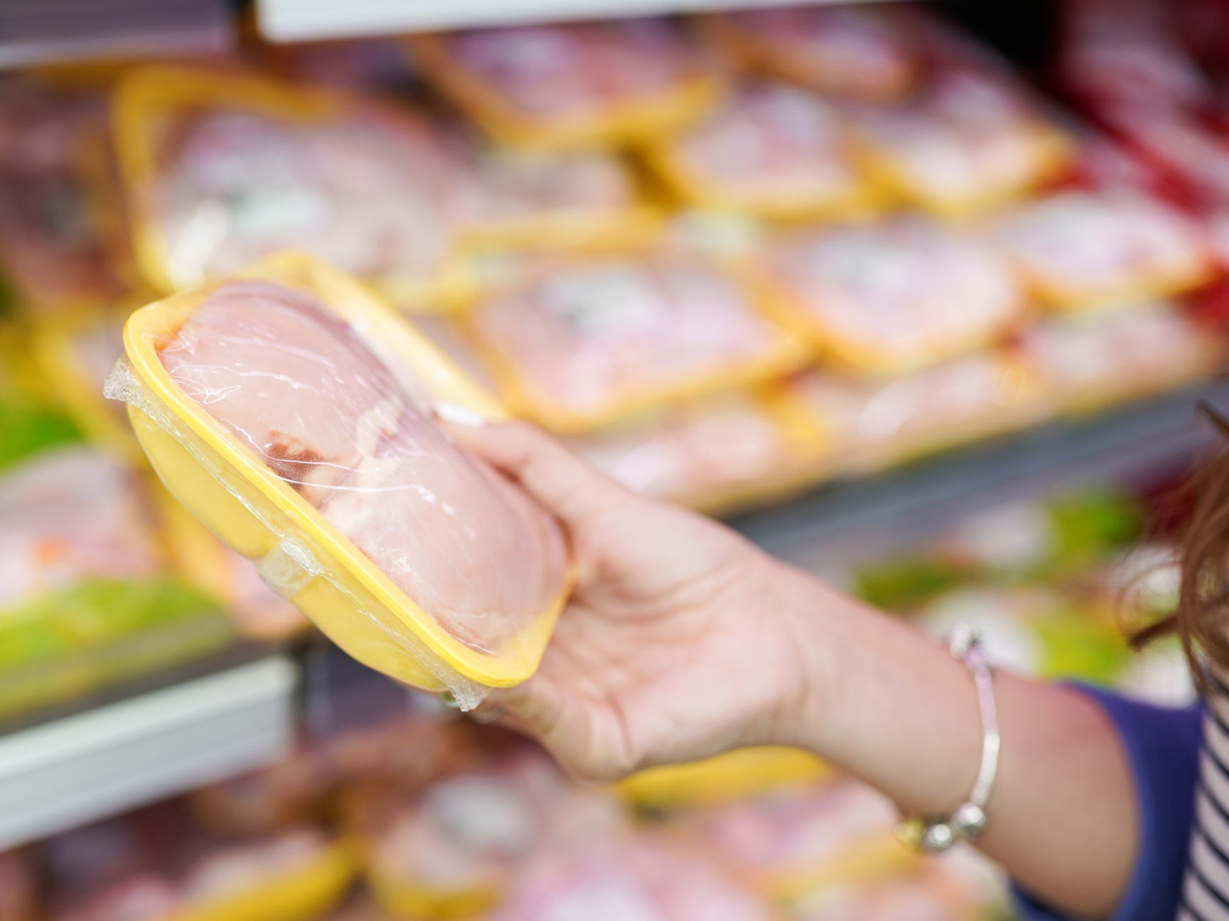 A person holding a package of raw chicken in a grocery store