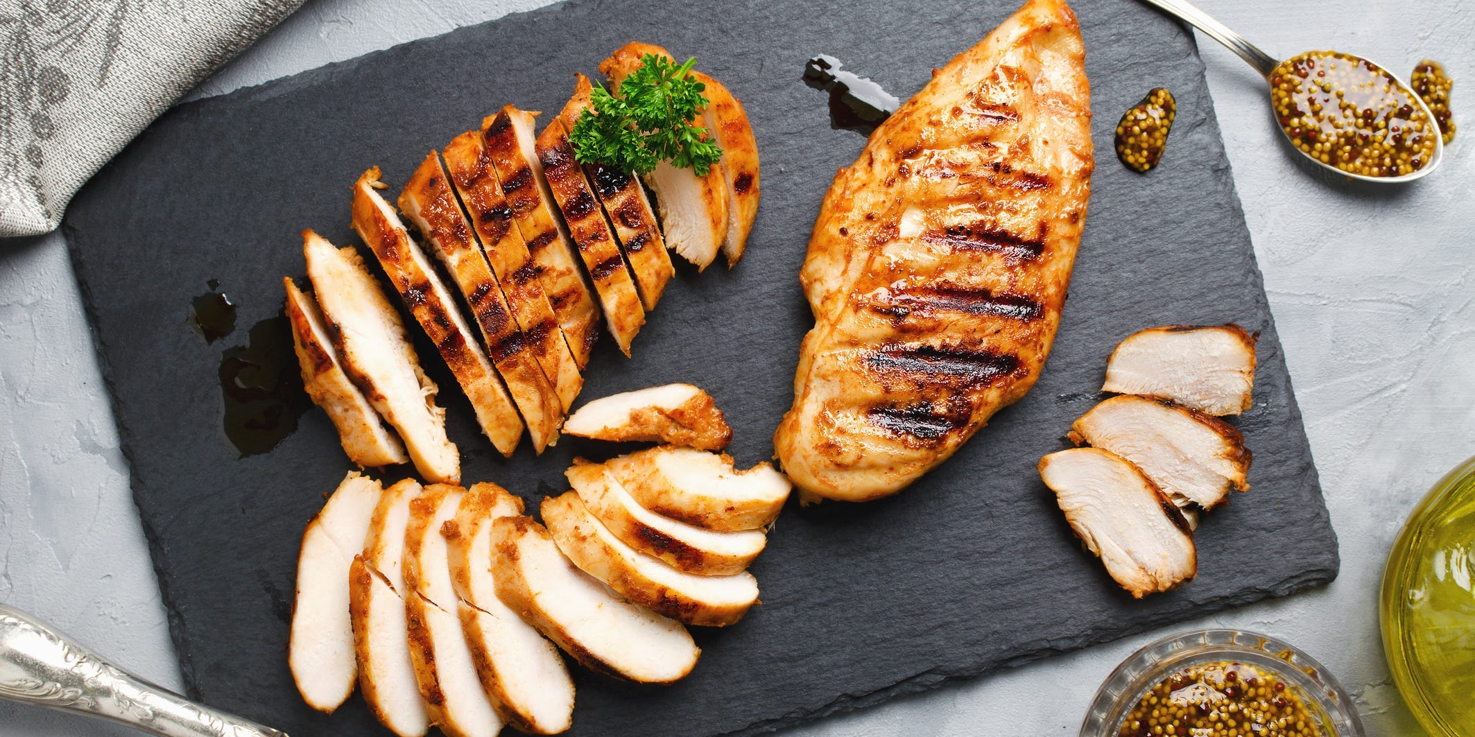 Grilled chicken sliced on a cutting board next to a whole chicken fillet