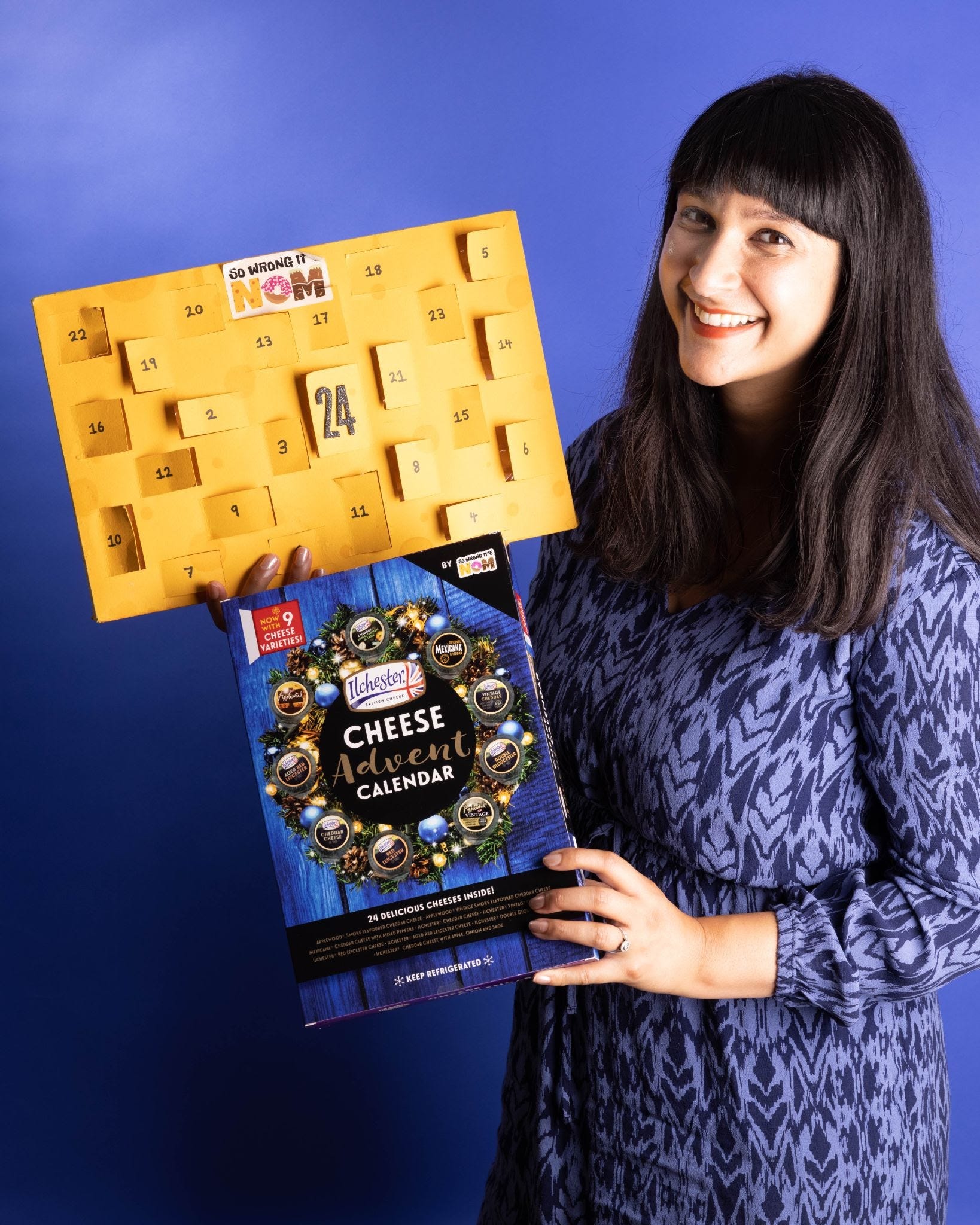Woman in purple dress against purple background holding cheese advent calendar