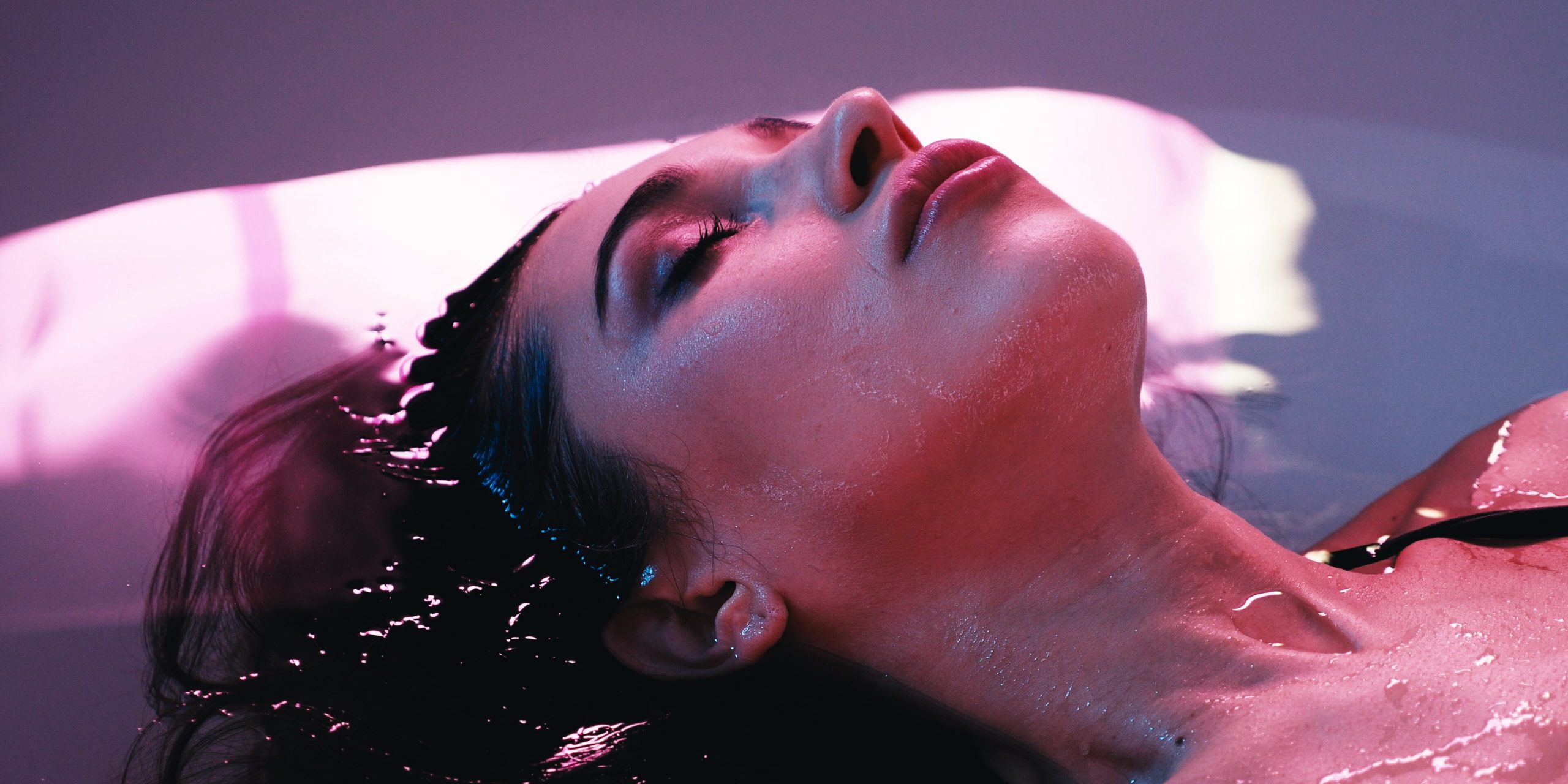 A young woman floats with her eyes closed in a sensory deprivation tank.