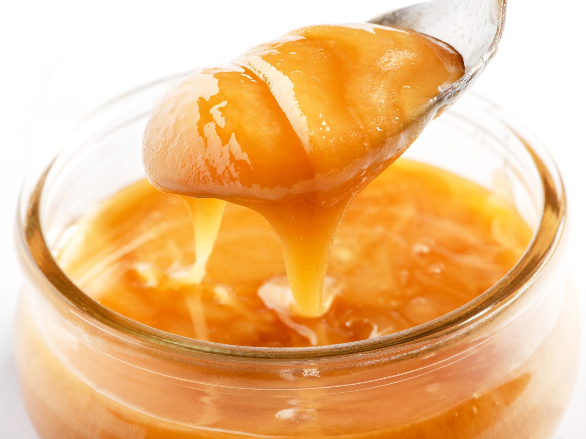 A spoon of crystallized thick honey being lifted from a jar.