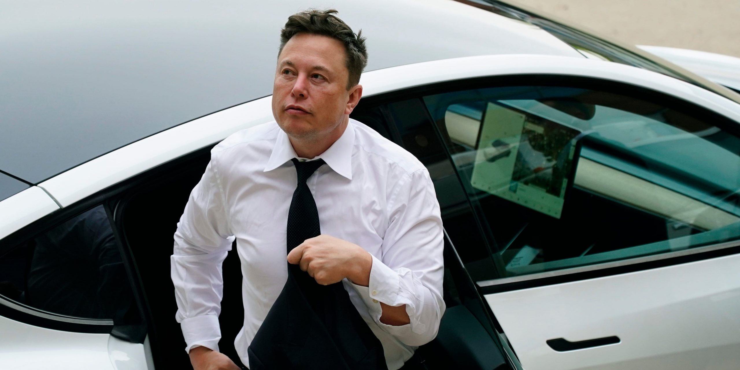 Tesla CEO Elon Musk in a white shirt and tie exits the backseat of a white Tesla