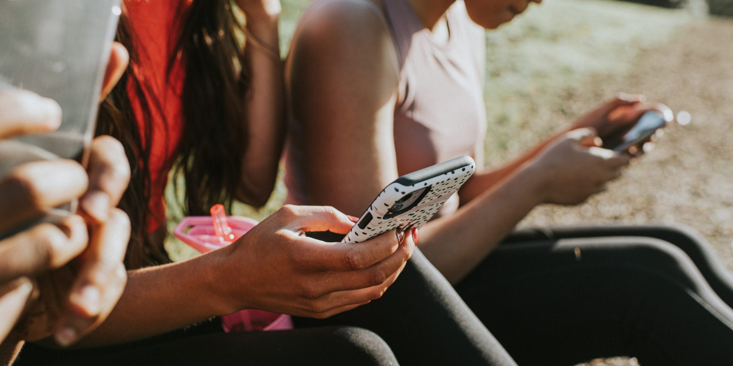 three women sitting on grass looking at phones