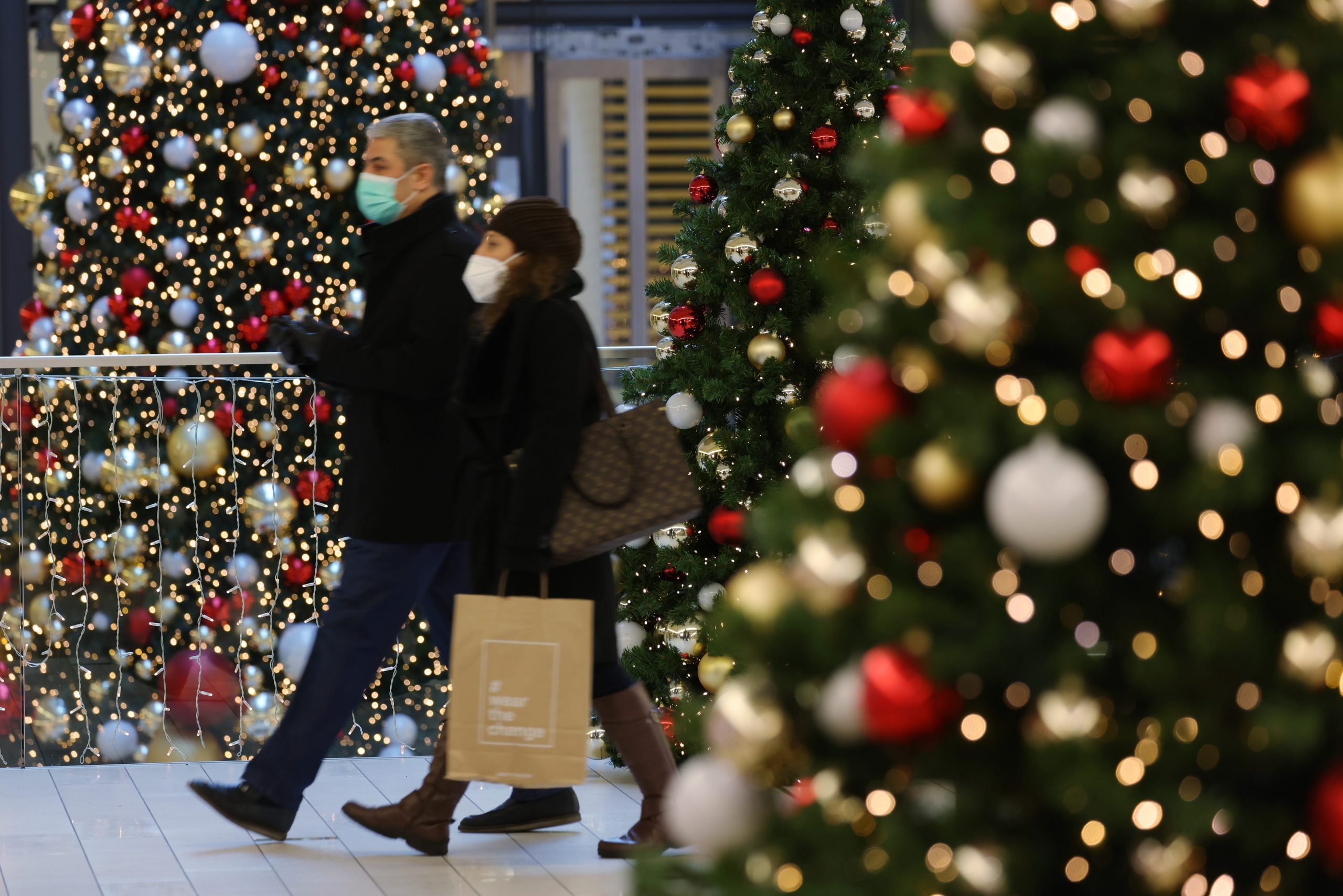Shoppers at a mall in Germany with Christmas trees decorated in red and gold around.