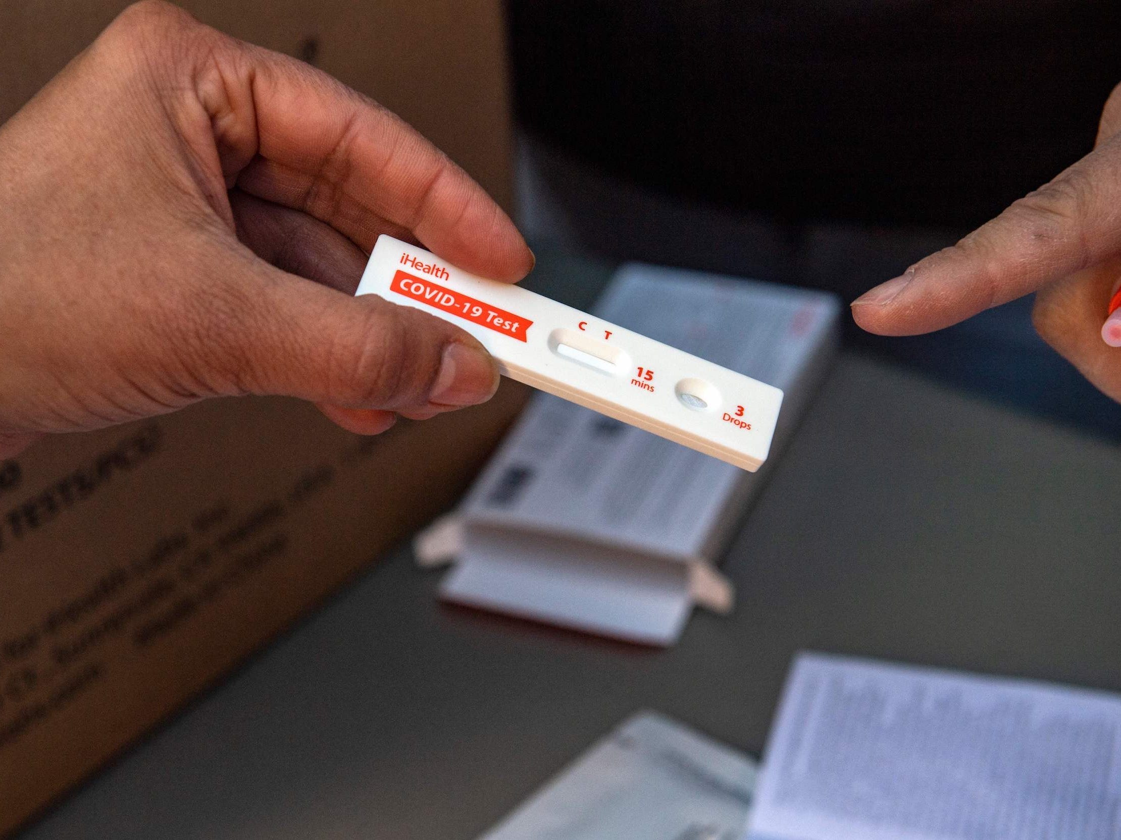 Hand holds at-home COVID-19 rapid test while finger points to results