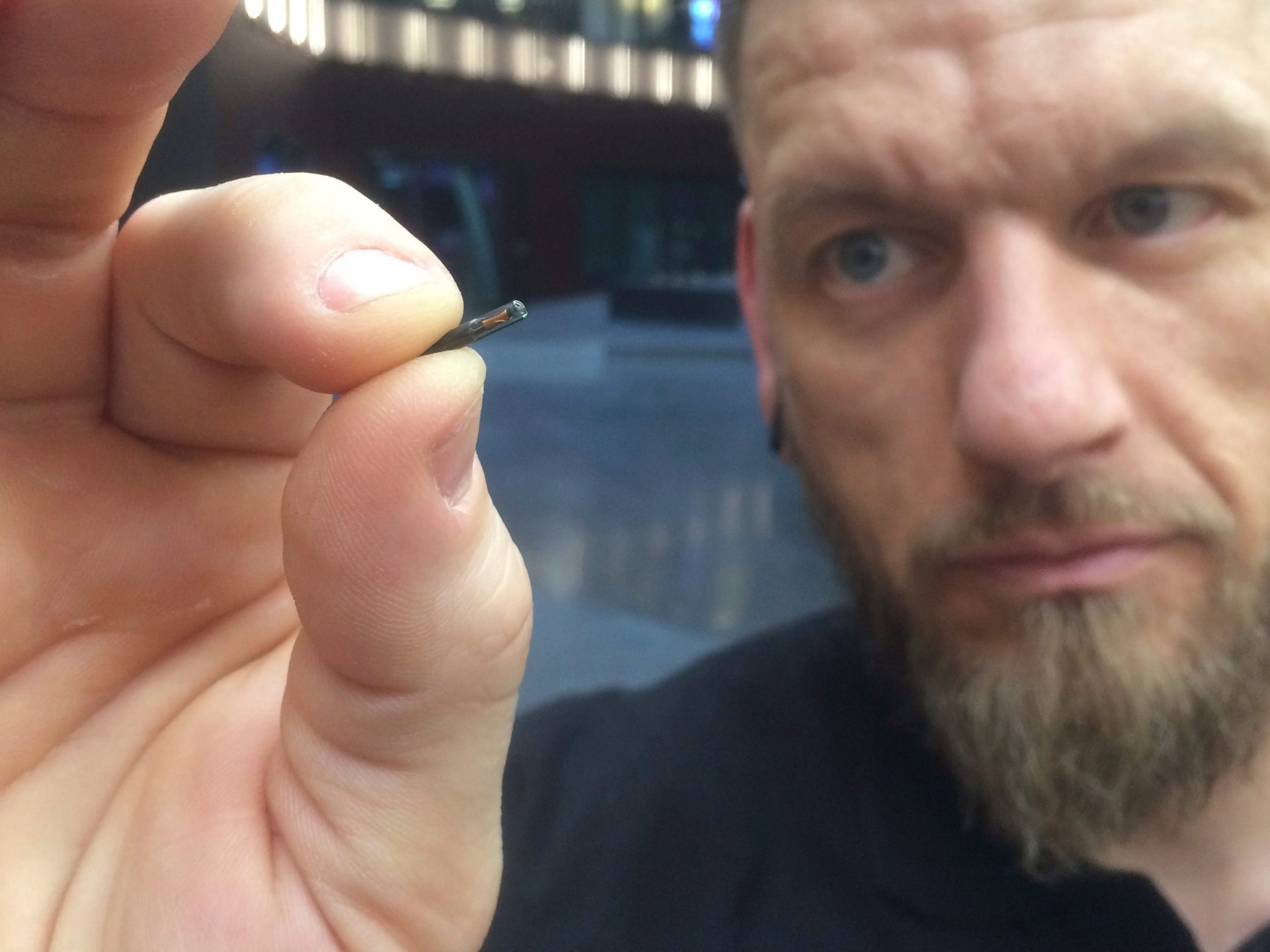 Man holds up a microchip implant the size of a grain.