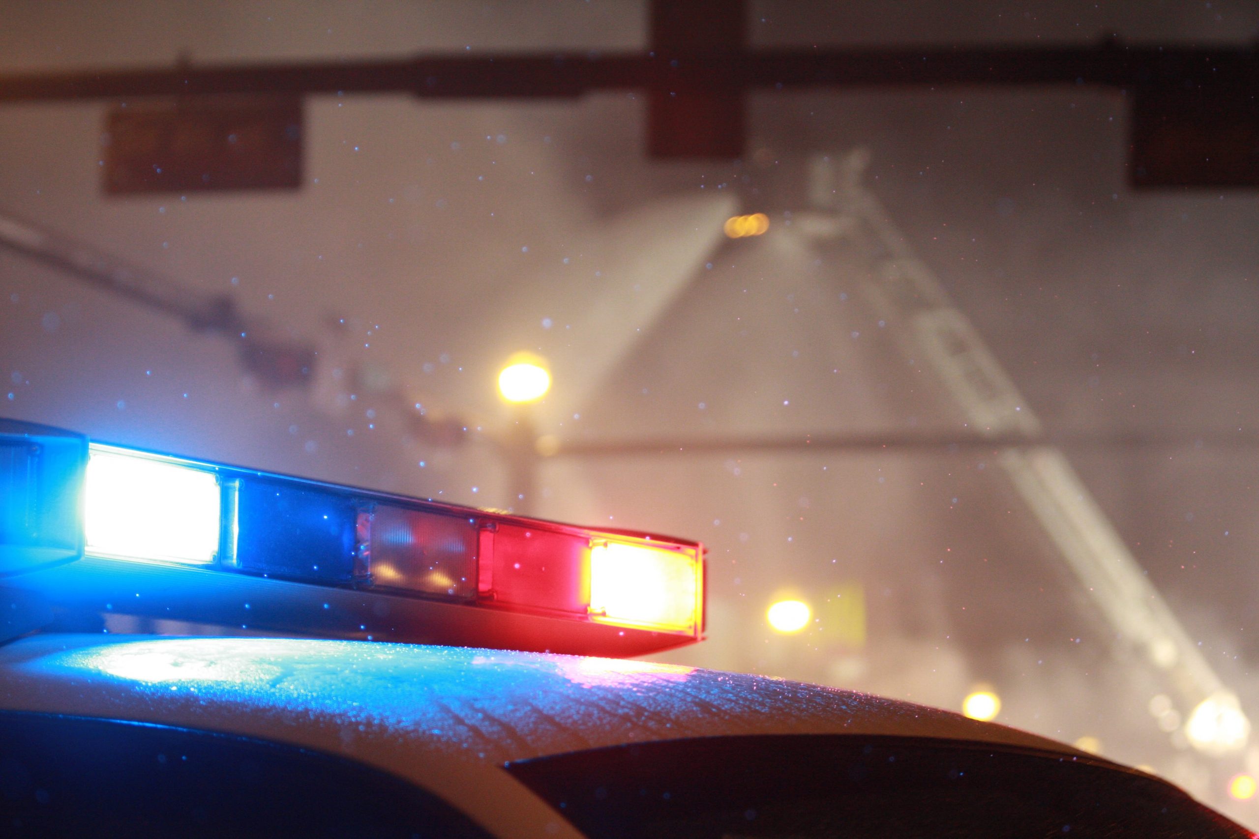 A lone police car stands guard as aerial and ground firemen battle a building fire in light snow.