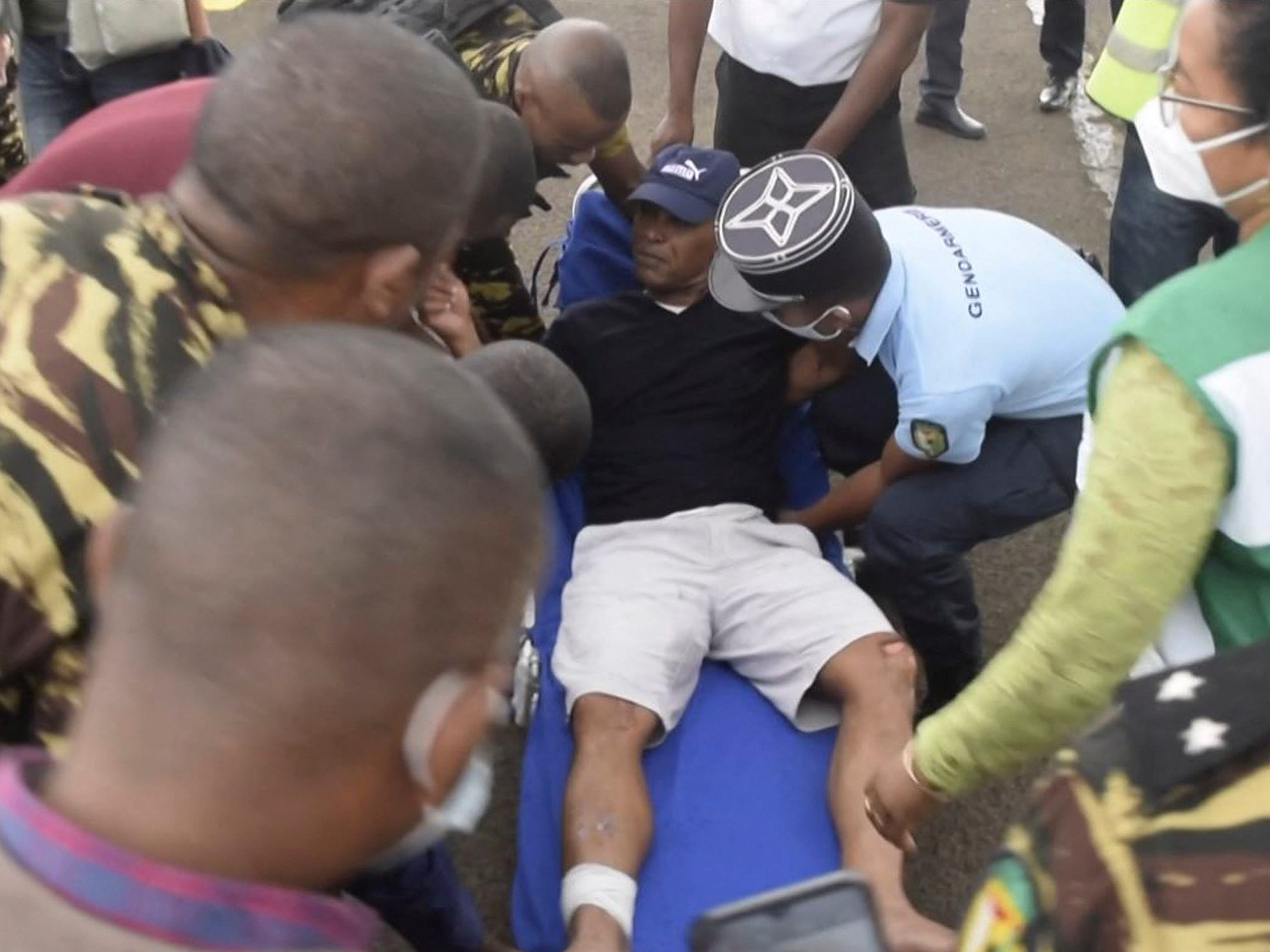 This video grab from an AFPTV video taken on December 21, 2021 shows General Serge Gelle (C), Secretary of State for police, transported on an emergency bed surrounded by soldiers on the runway to the plane in Antananarivo.