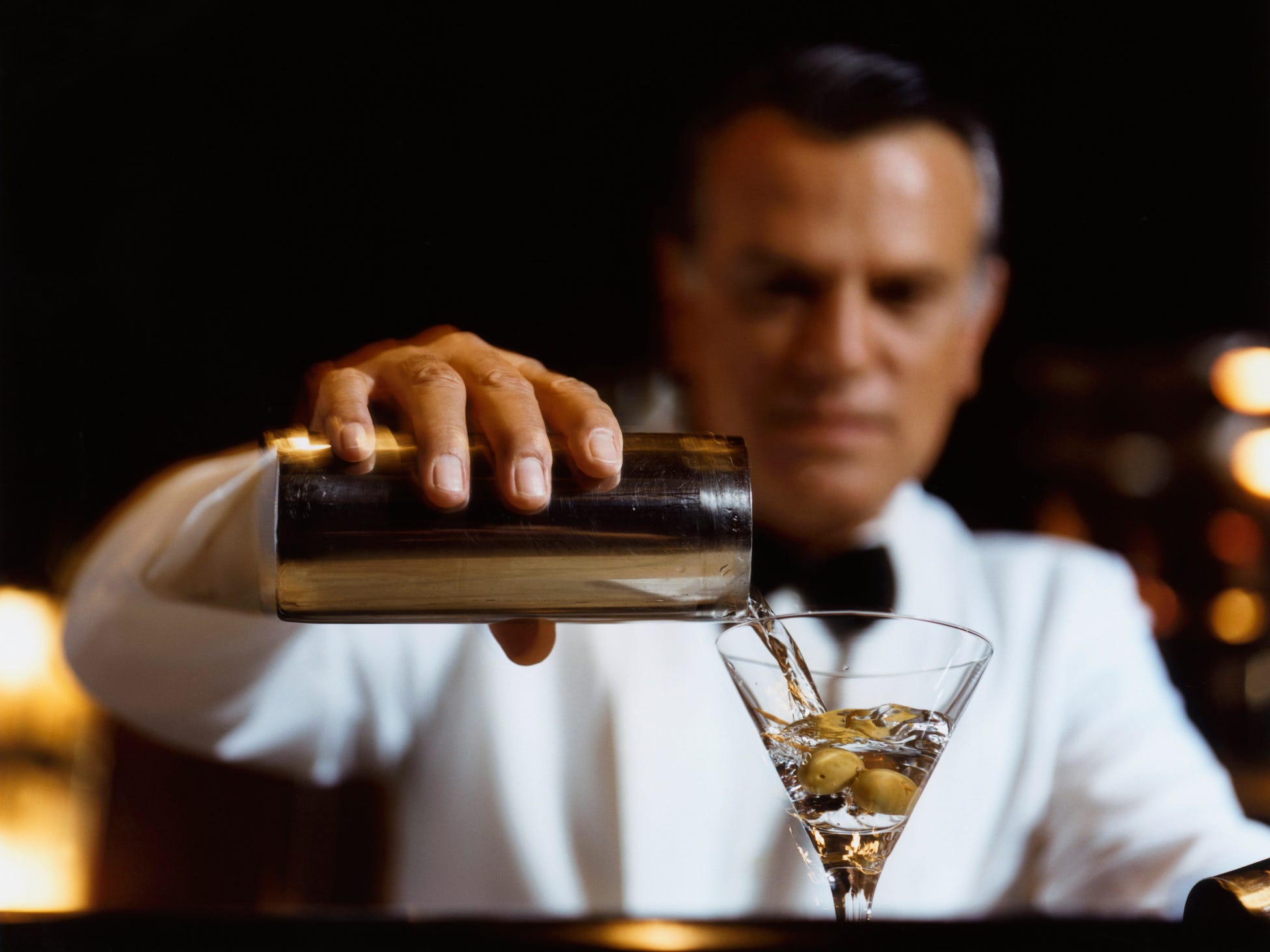 A bartender pouring a martini into a glass with an olive at the bottom.