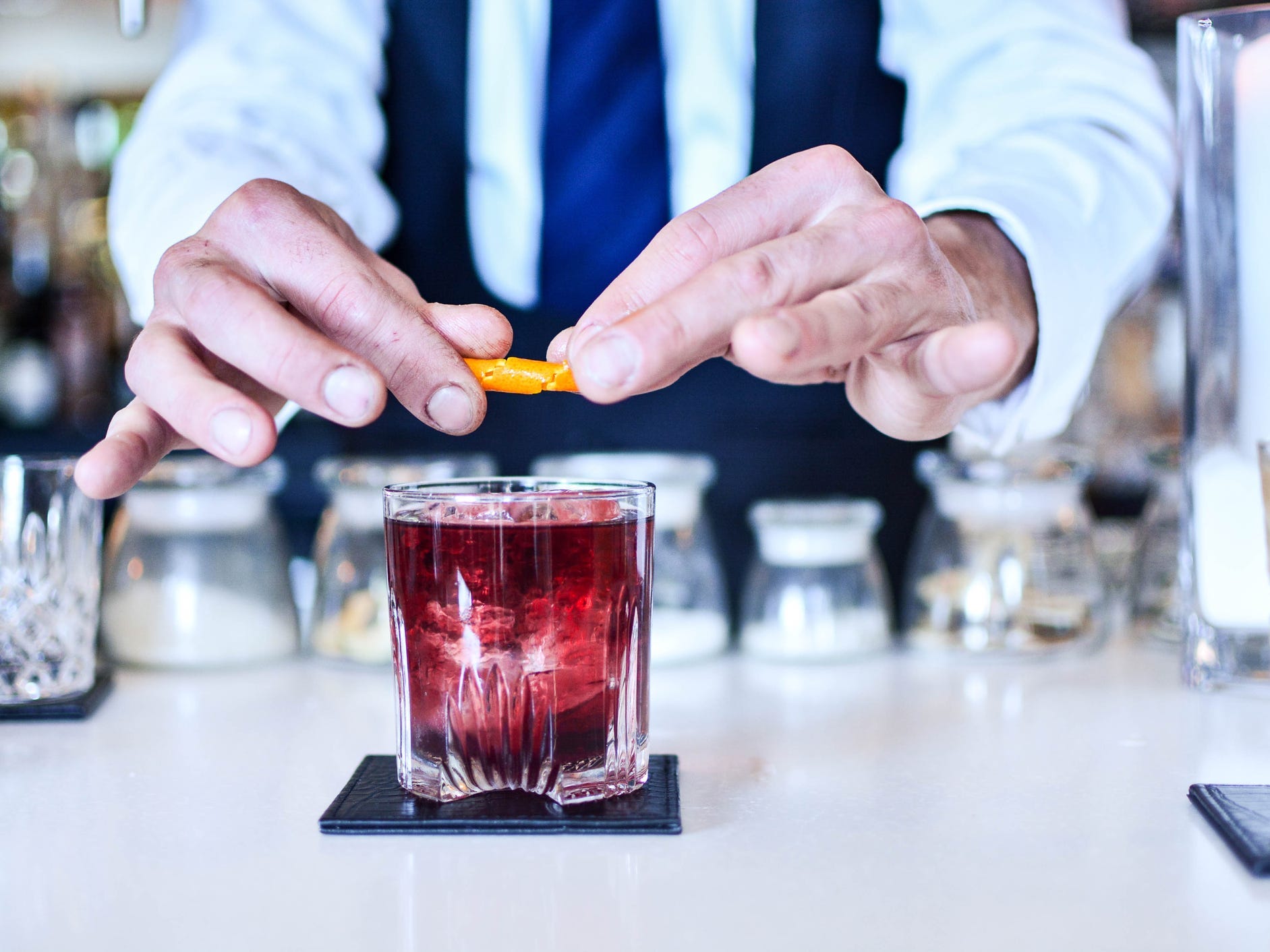 A bartender making a Negroni cocktail with an orange peel garnish.