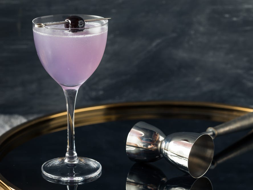 A glass of purple aviation cocktail on a gold tray.