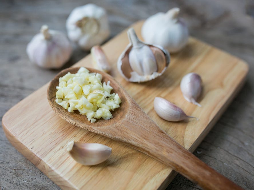 A wood spoon full of minced garlic with bulbs and cloves of garlic in the background.