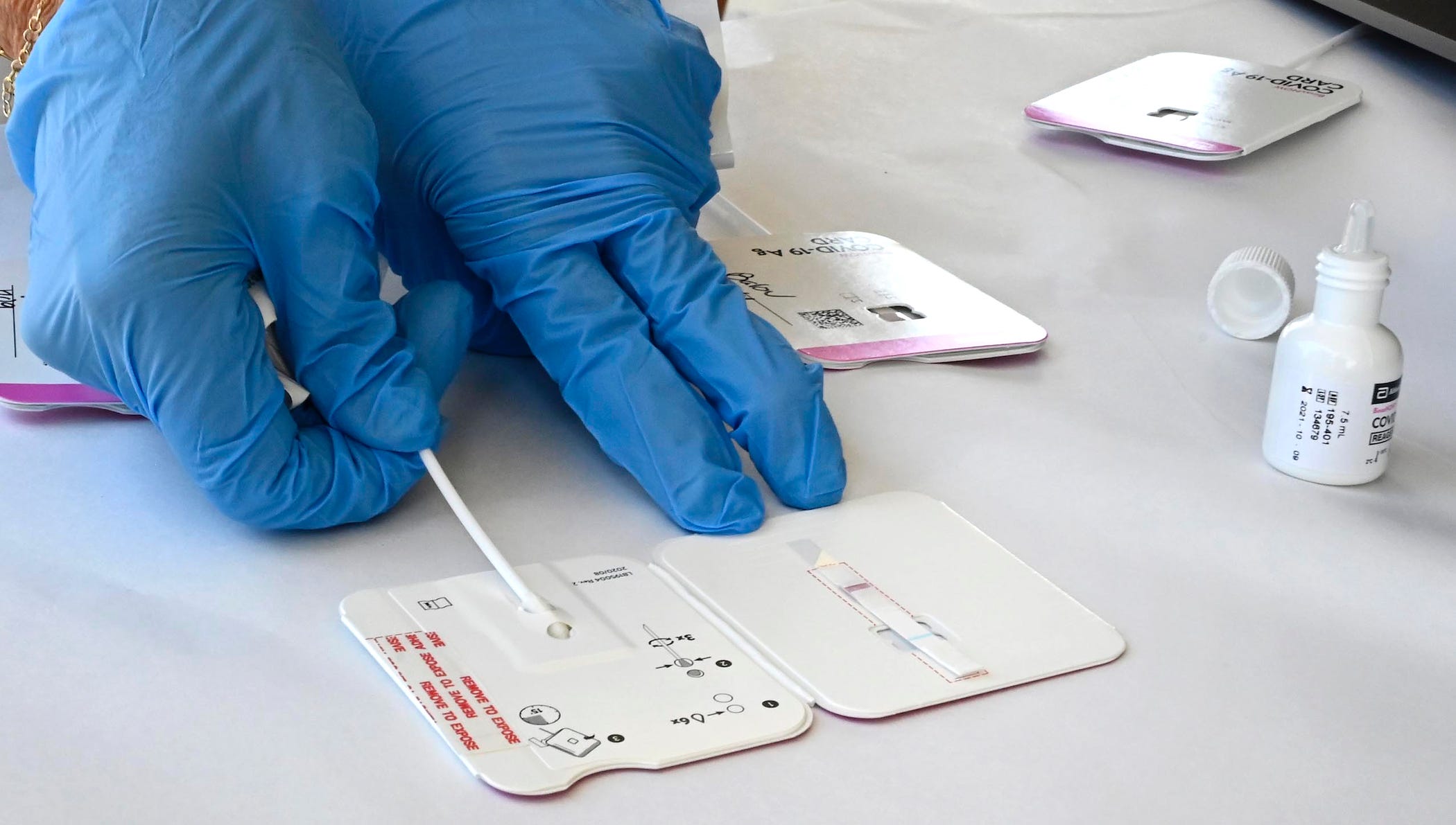 gloved person inserting rapid test swab into binax now card