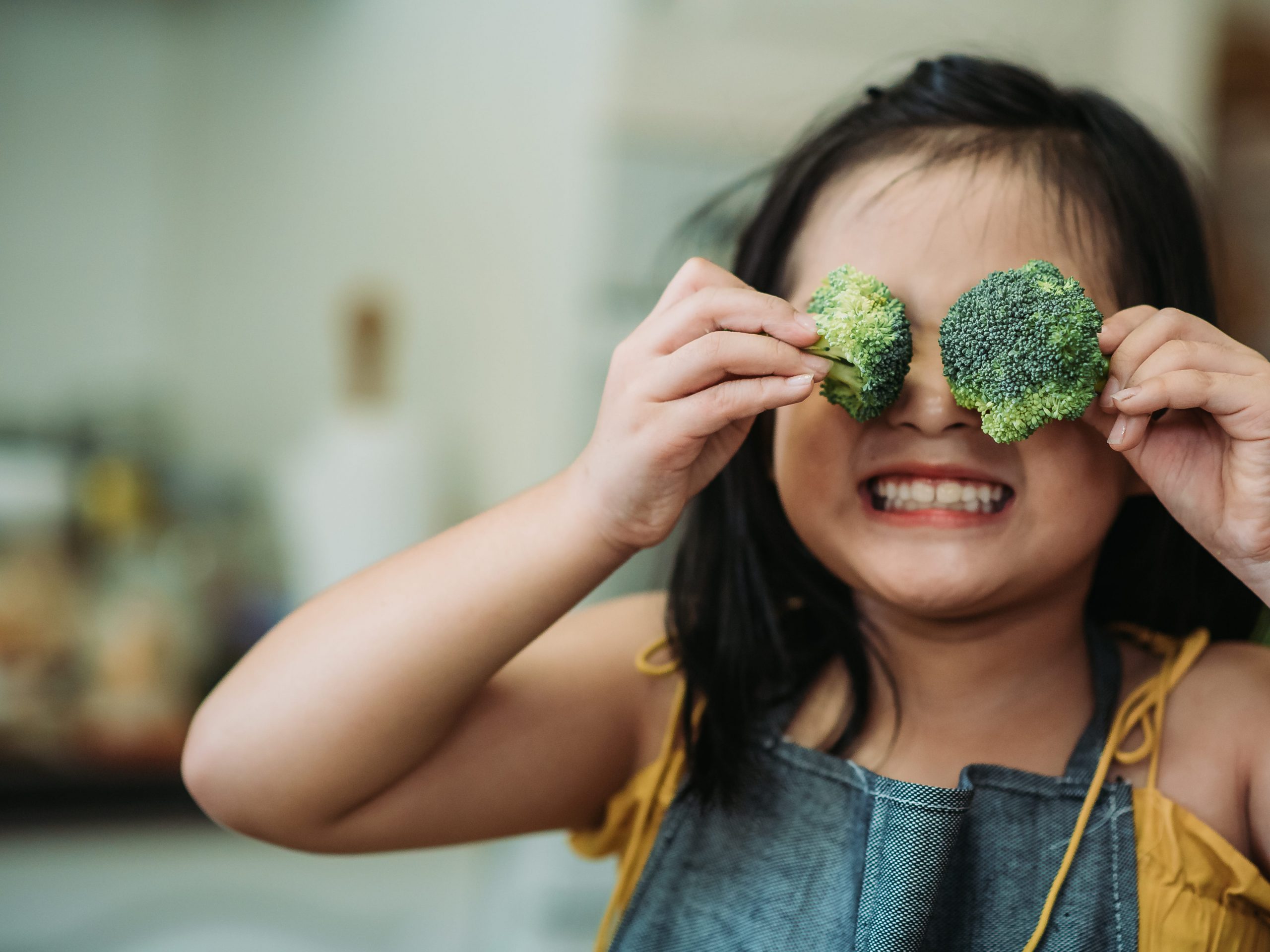 child act cute with hand holding broccoli putting in front of her eyes with smiling face at kitchen