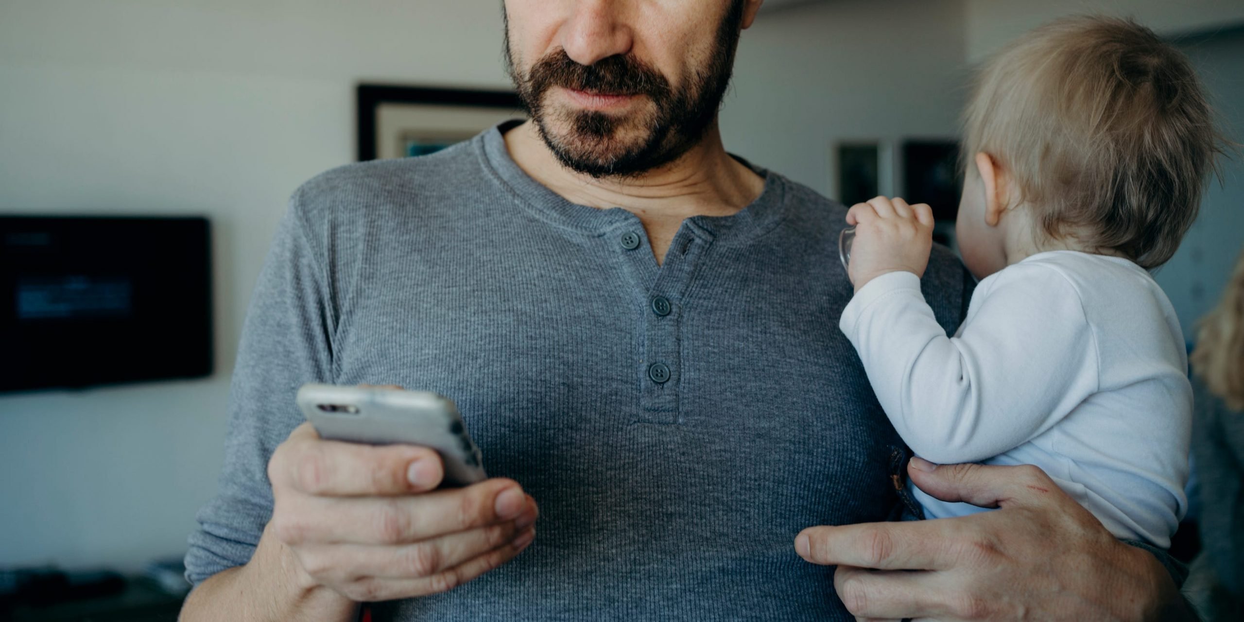 A man holding a baby and staring at an iPhone.