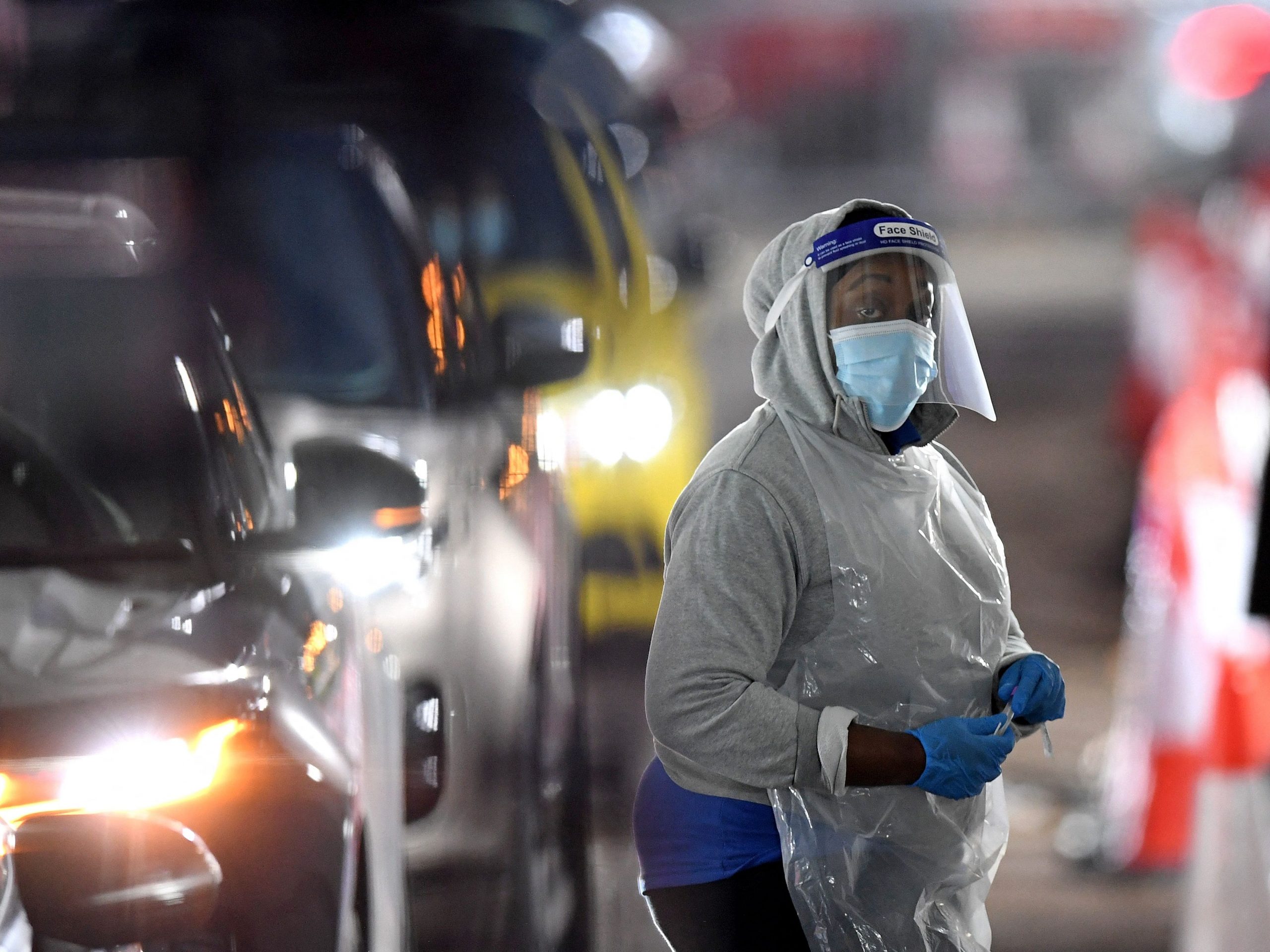 Woman with personal protective equipment working at drive through COVID-19 testing site.