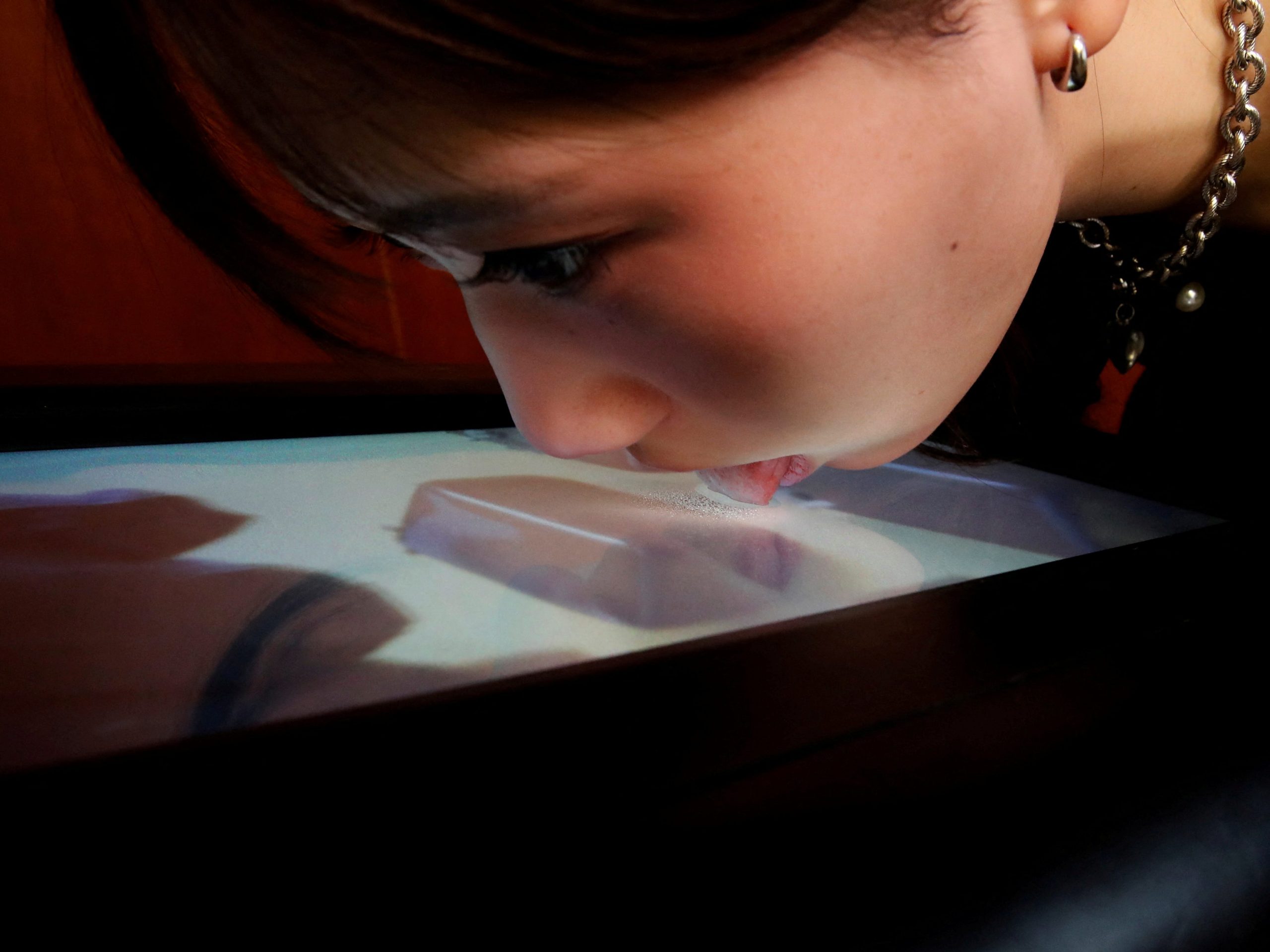 A woman licks the screen of Taste The TV, the prototype of a lickable TV screen.