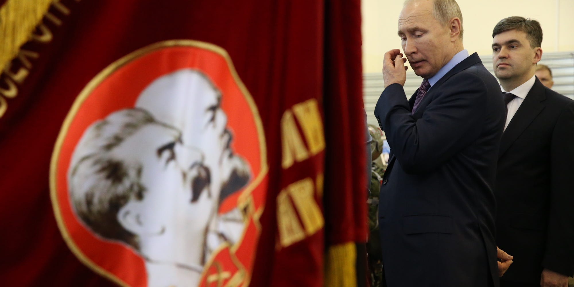 Russian President Vladimir Putin next to a flag with the images of Joseph Stalin and Vladimir Lenin.