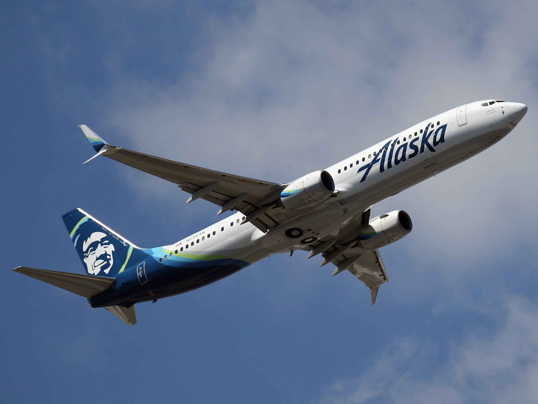An Alaska Airlines airplane taking off against a blue sky with white clouds.